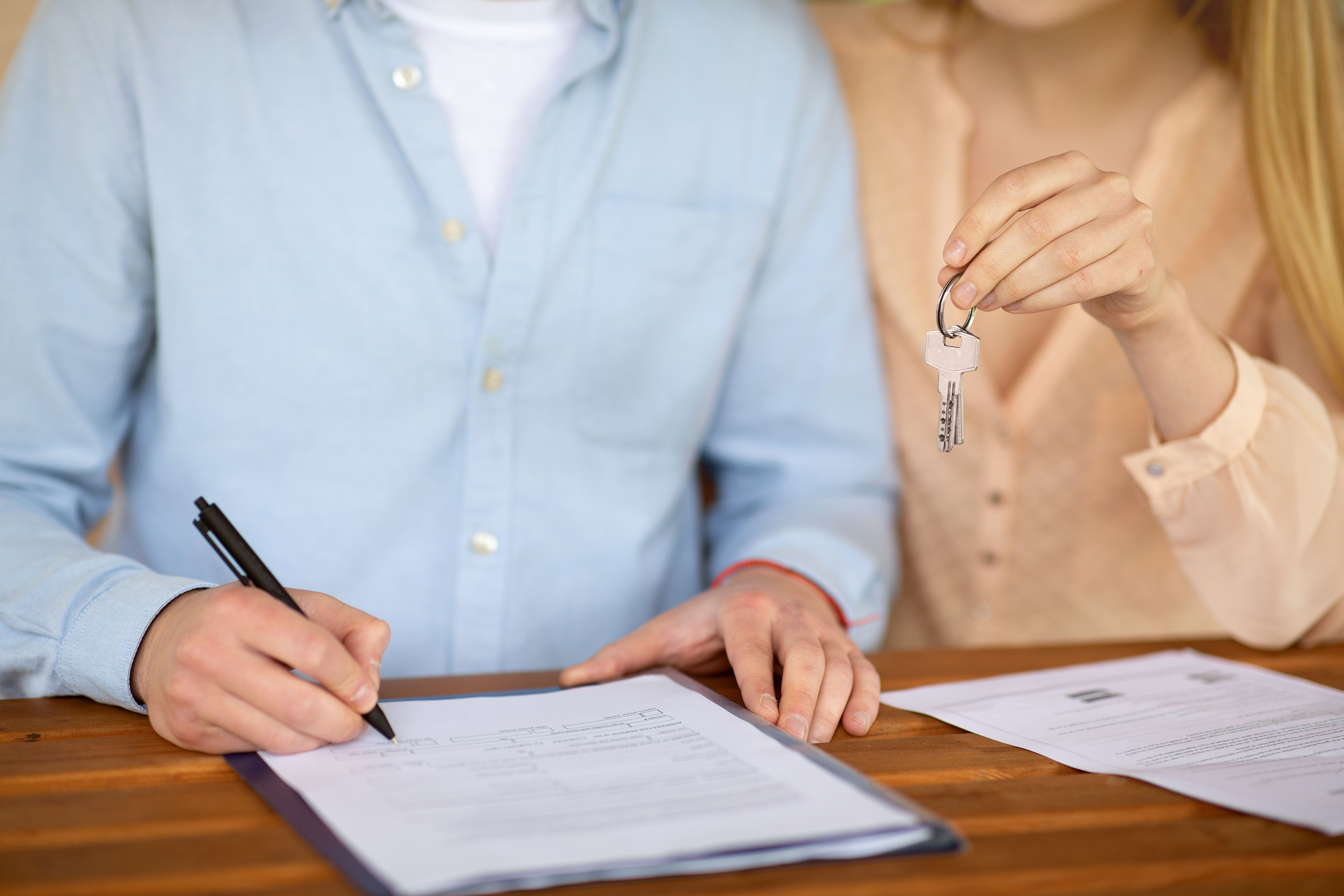 A closeup view of a young couple with house key, signing an agreement on a table
