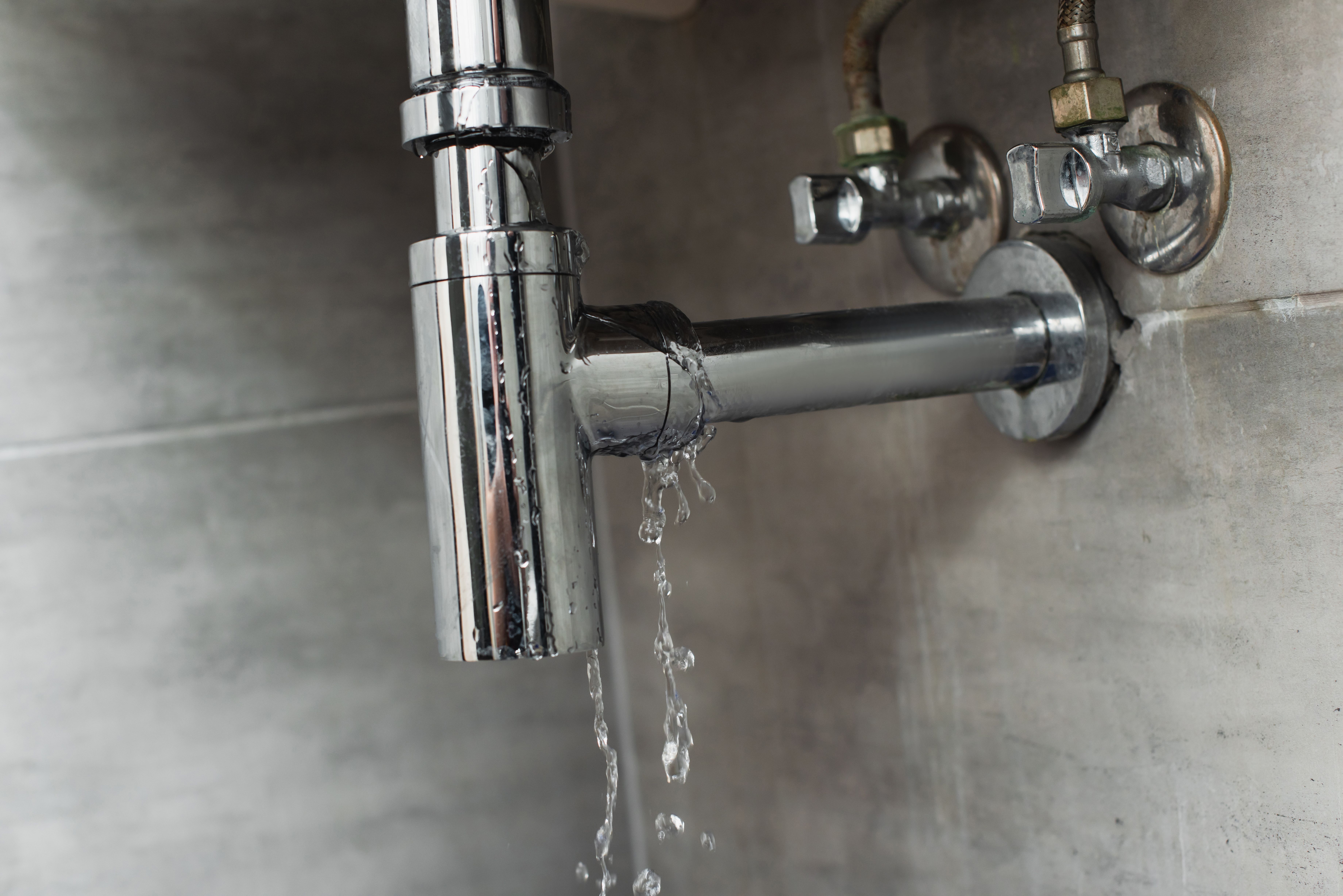 A damaged pipe with leaking water on grey background