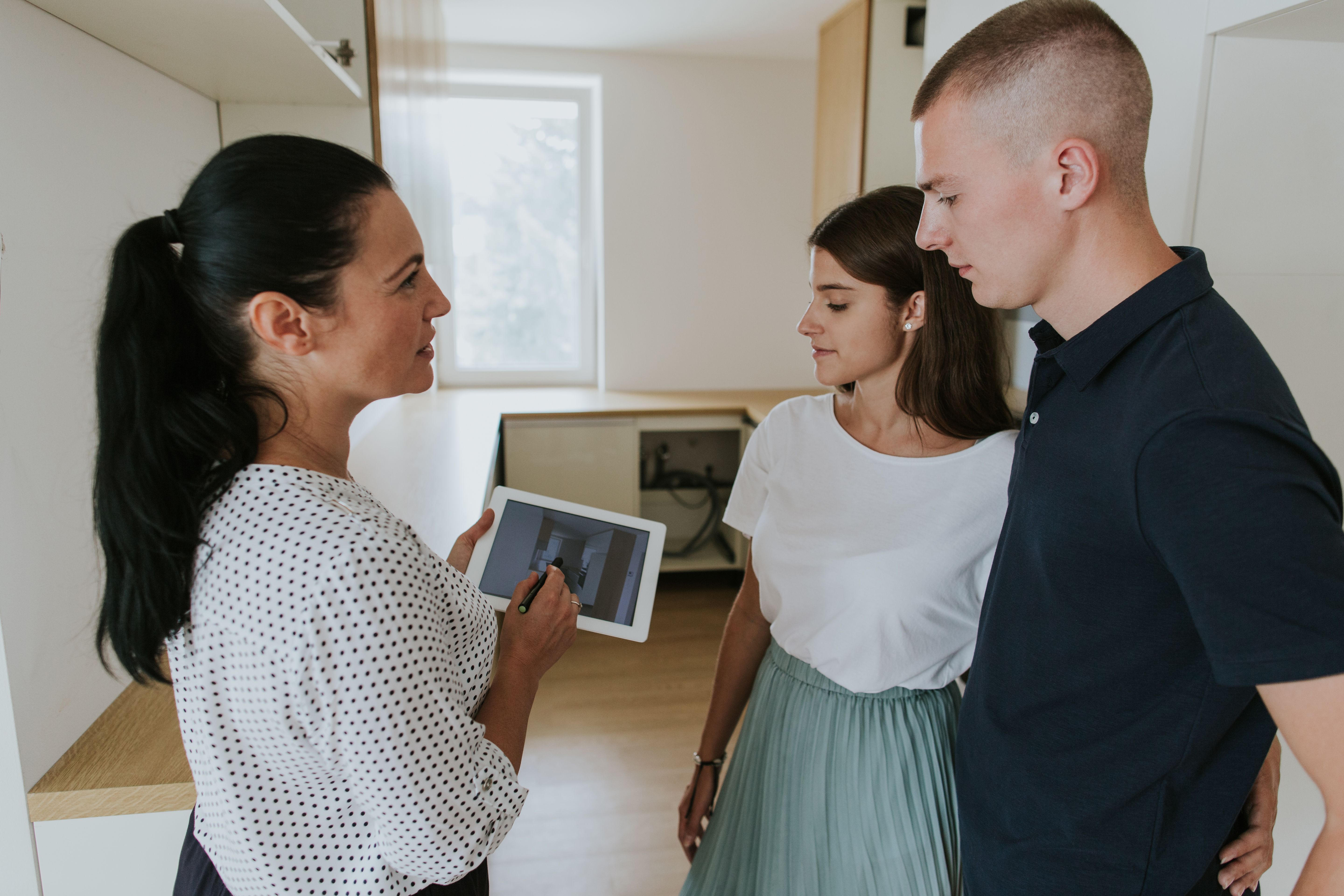 During a property viewing, a female real estate agent is showing first-time buyers using a digital tablet 
