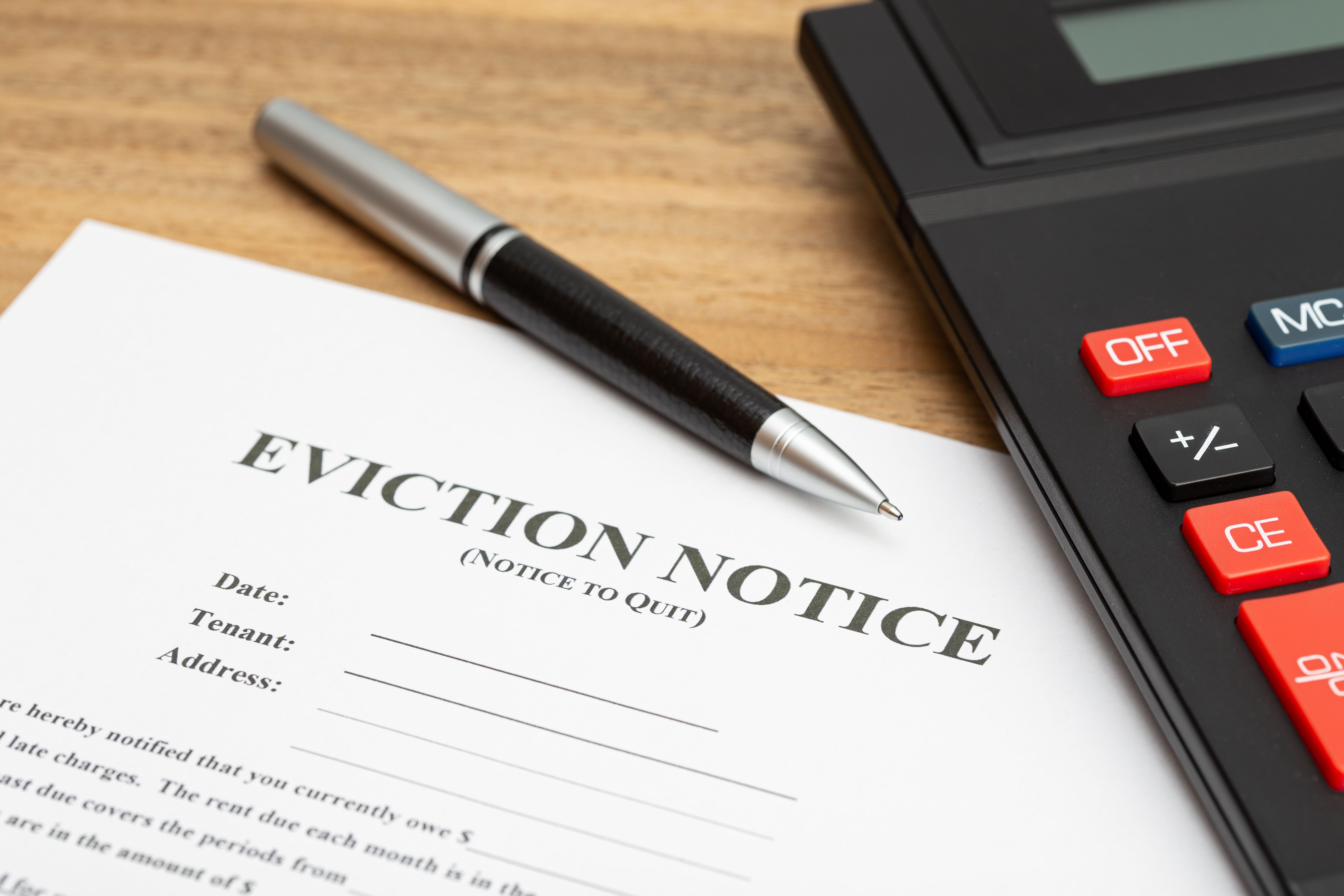 A sheet of eviction note on a wooden table under a pen and a calculator with black and metal exterior.jpg