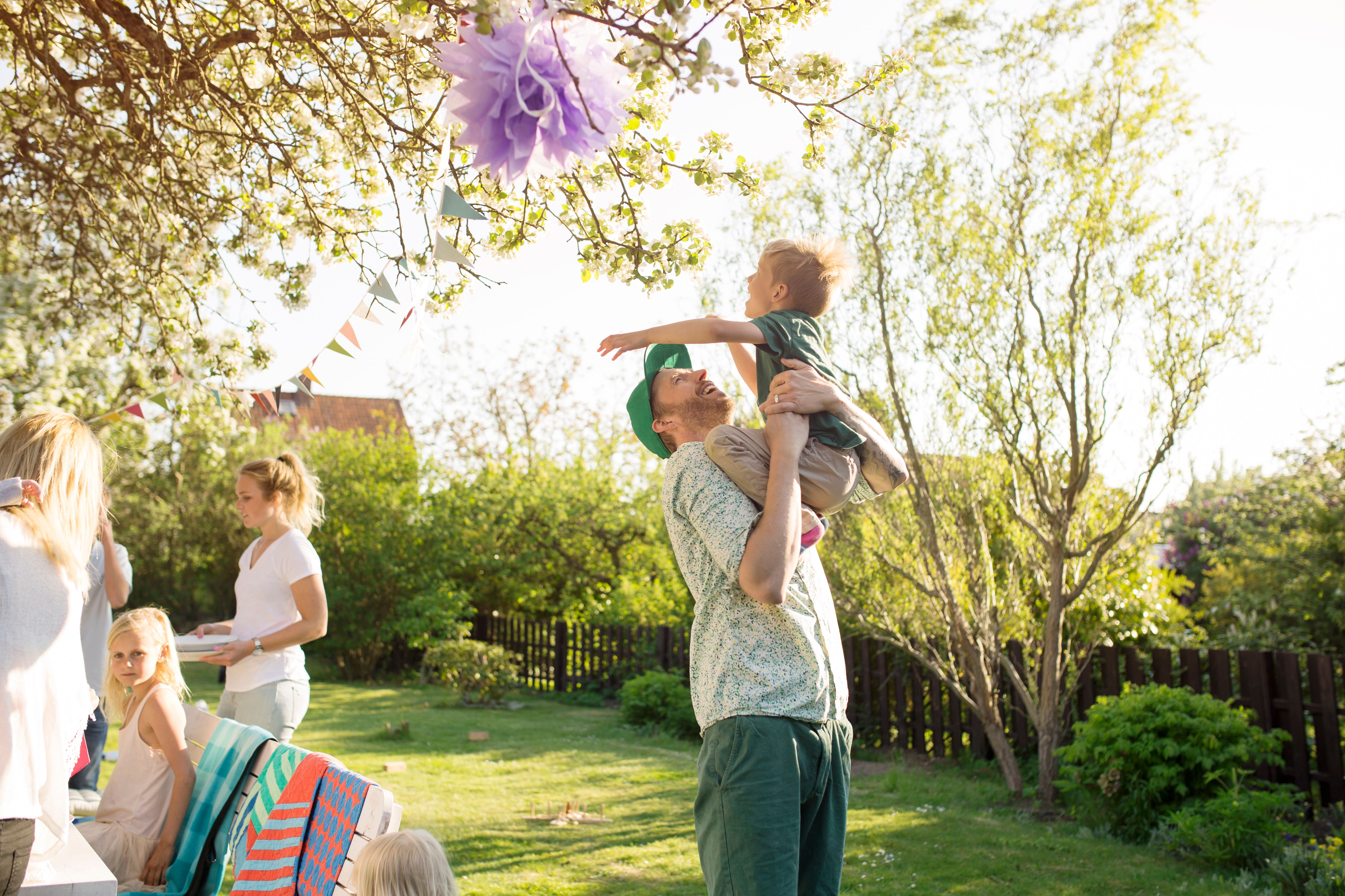 A man lifting a boy in a large communal garden with a child and two
women in the background