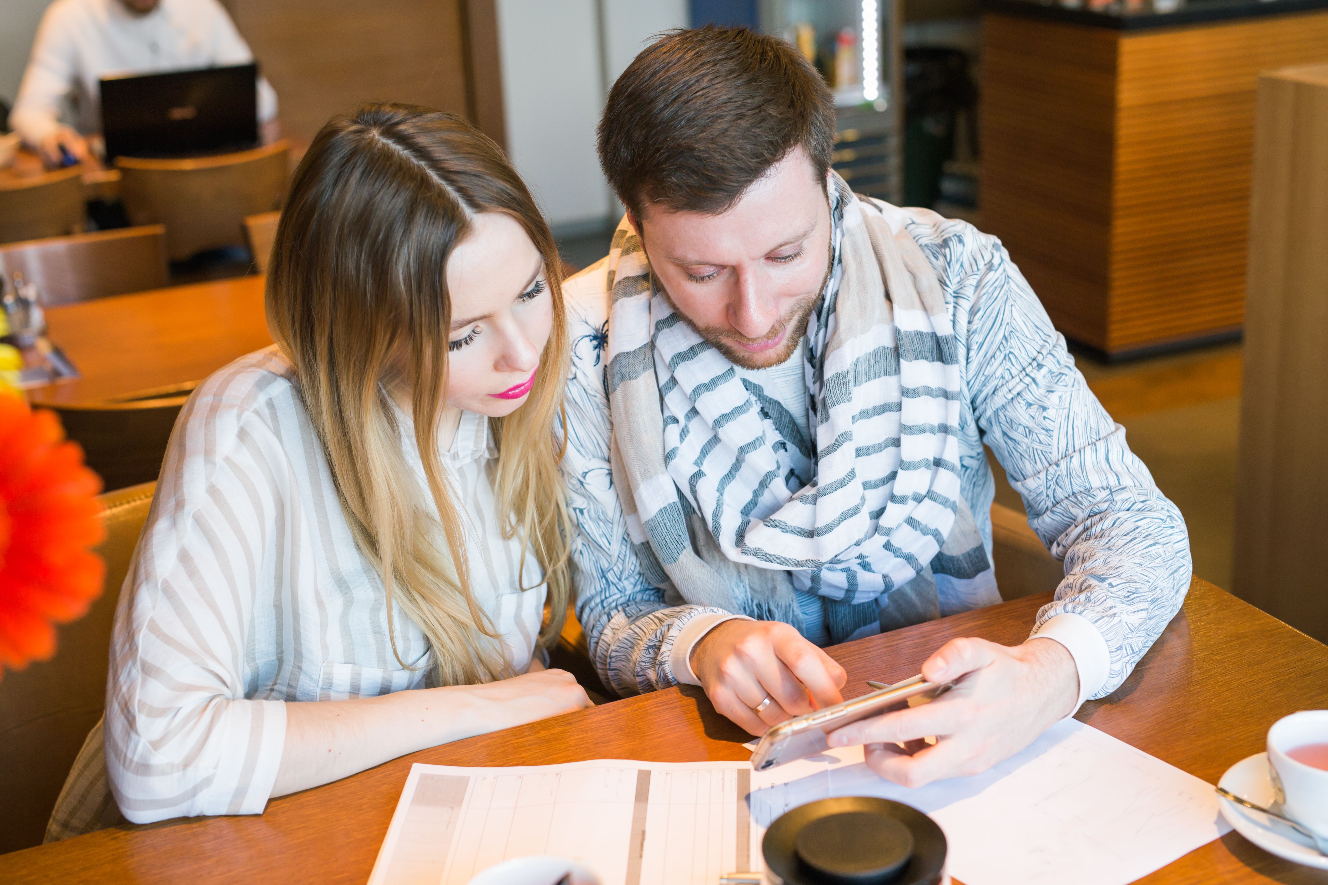 A man and a woman looking at a phone with documents and a coffee cup on their table