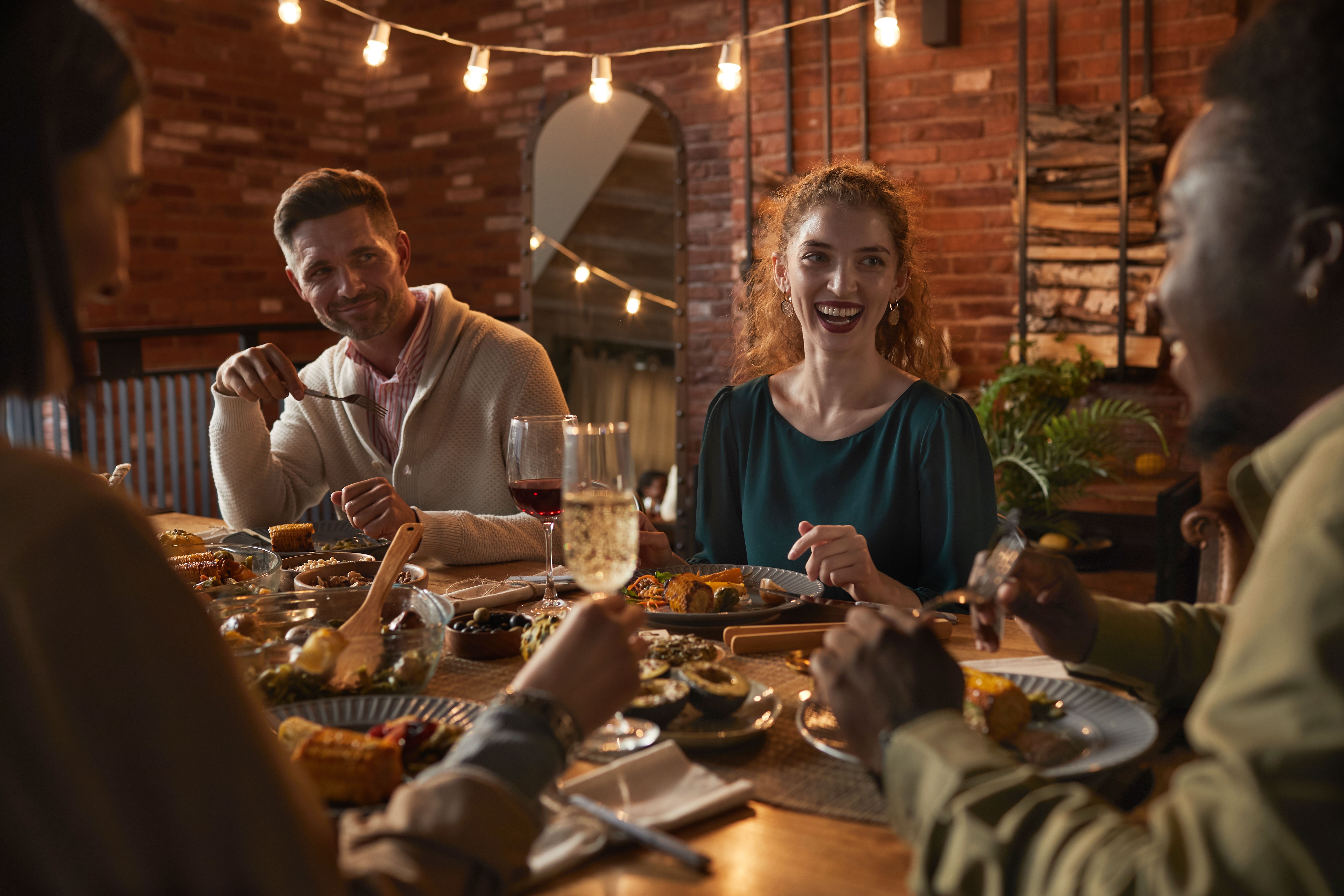 A group of friends enjoying a dinner party with wine and food on the table and a plant in the background