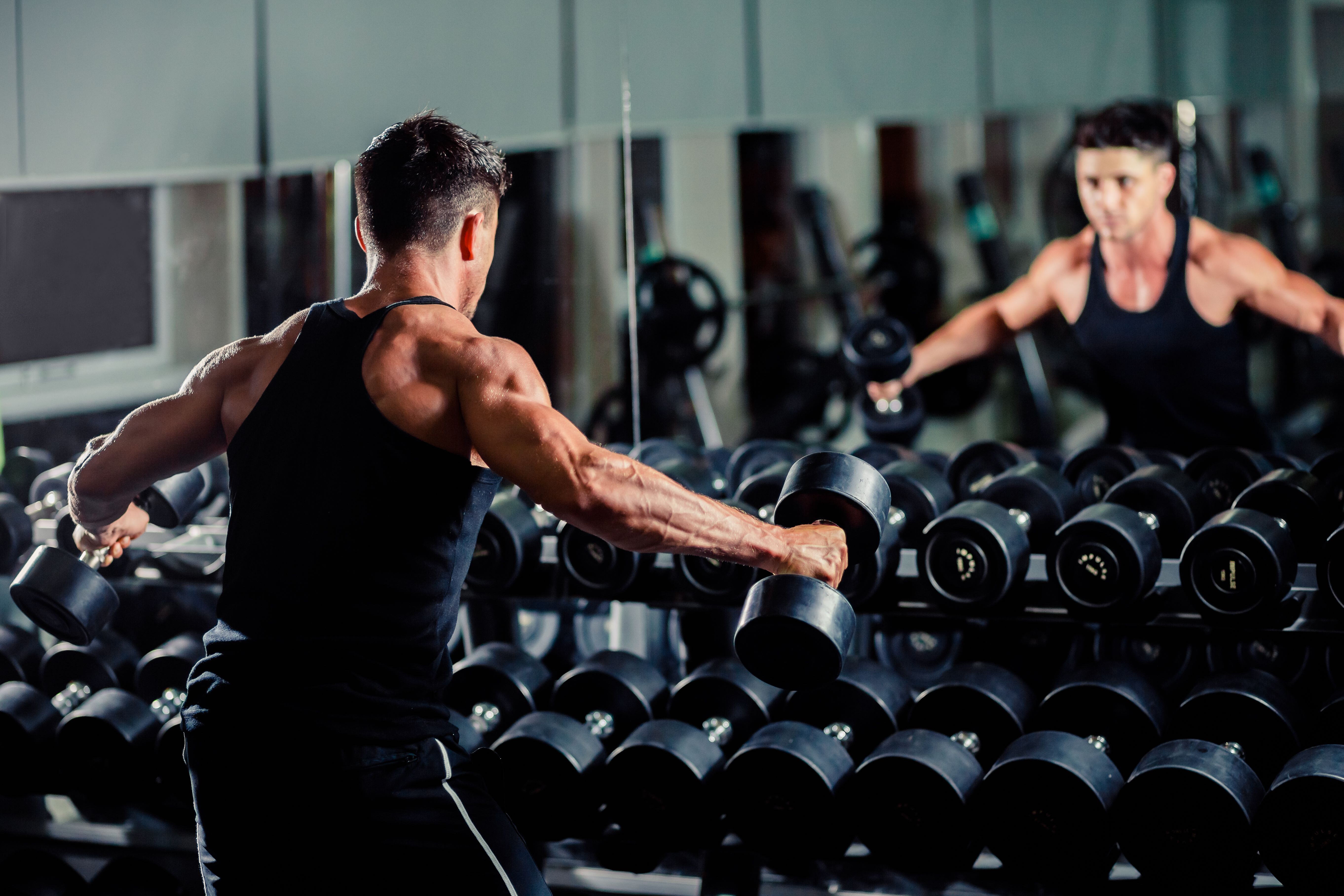 A man standing in front of a mirror and exercising with dumbbells with a row of dumbbells before him 