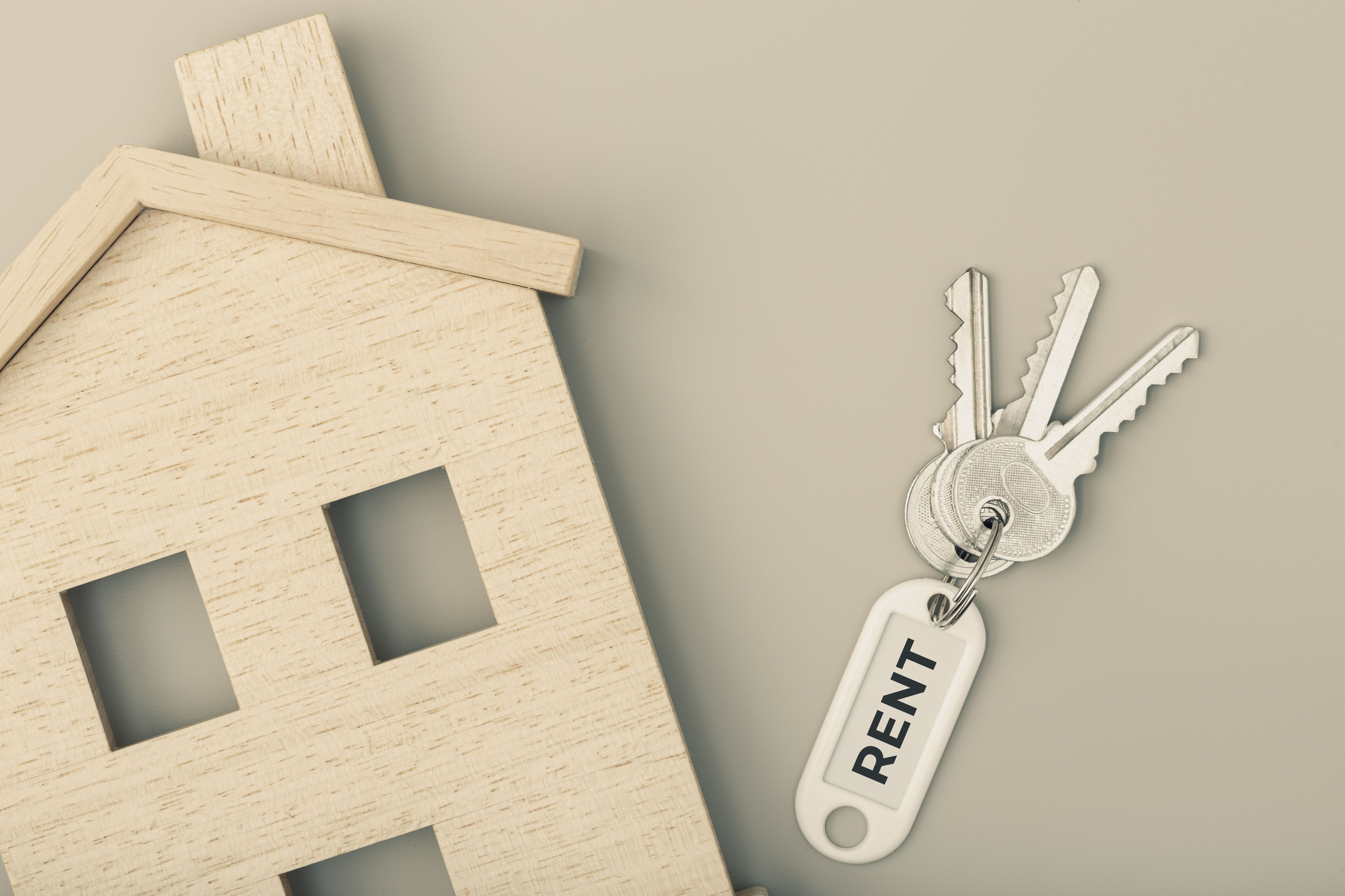 A set of 3 keys for a rental property with a white "Rent" tag, on the right of a veneer wooden house model with two windows and one door.