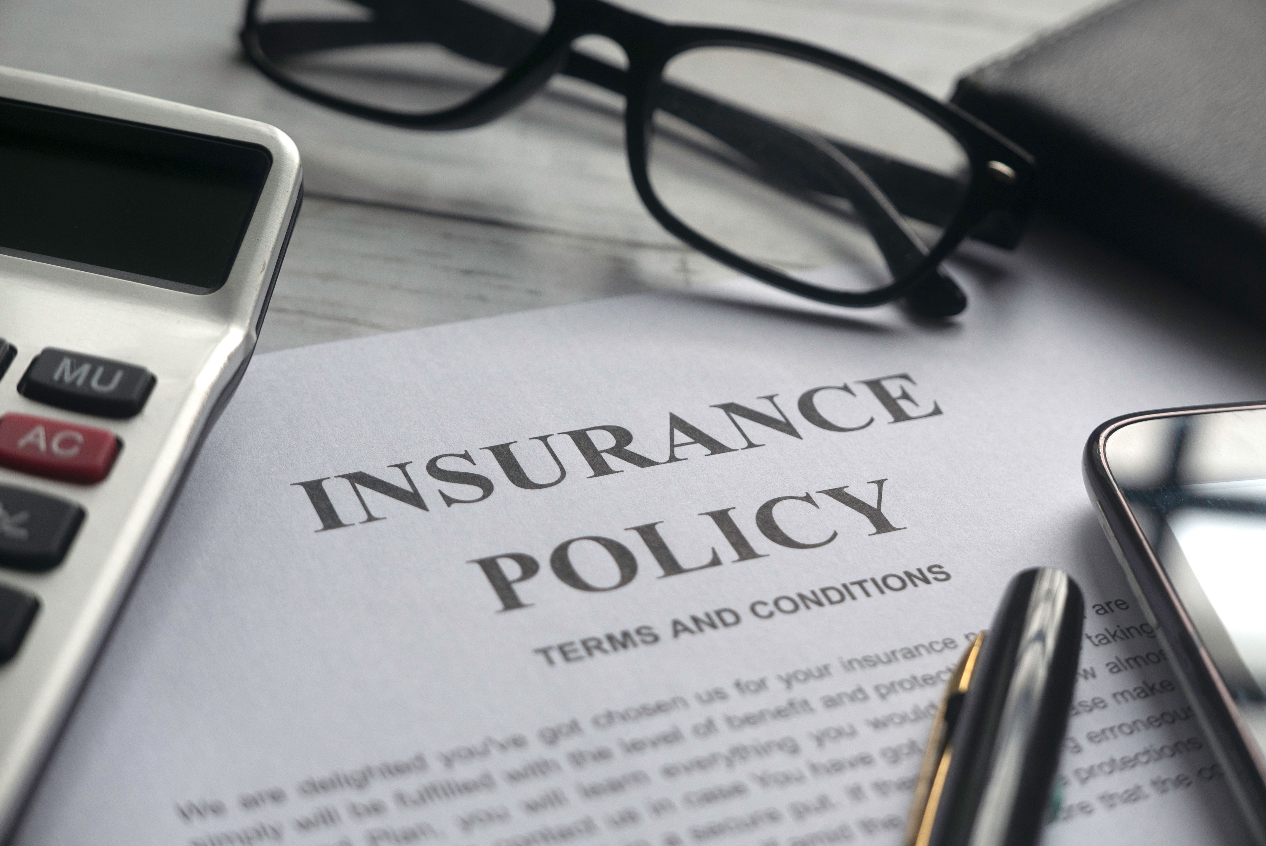 An insurance policy document with a pen, a calculator, and a pair of glasses on a table