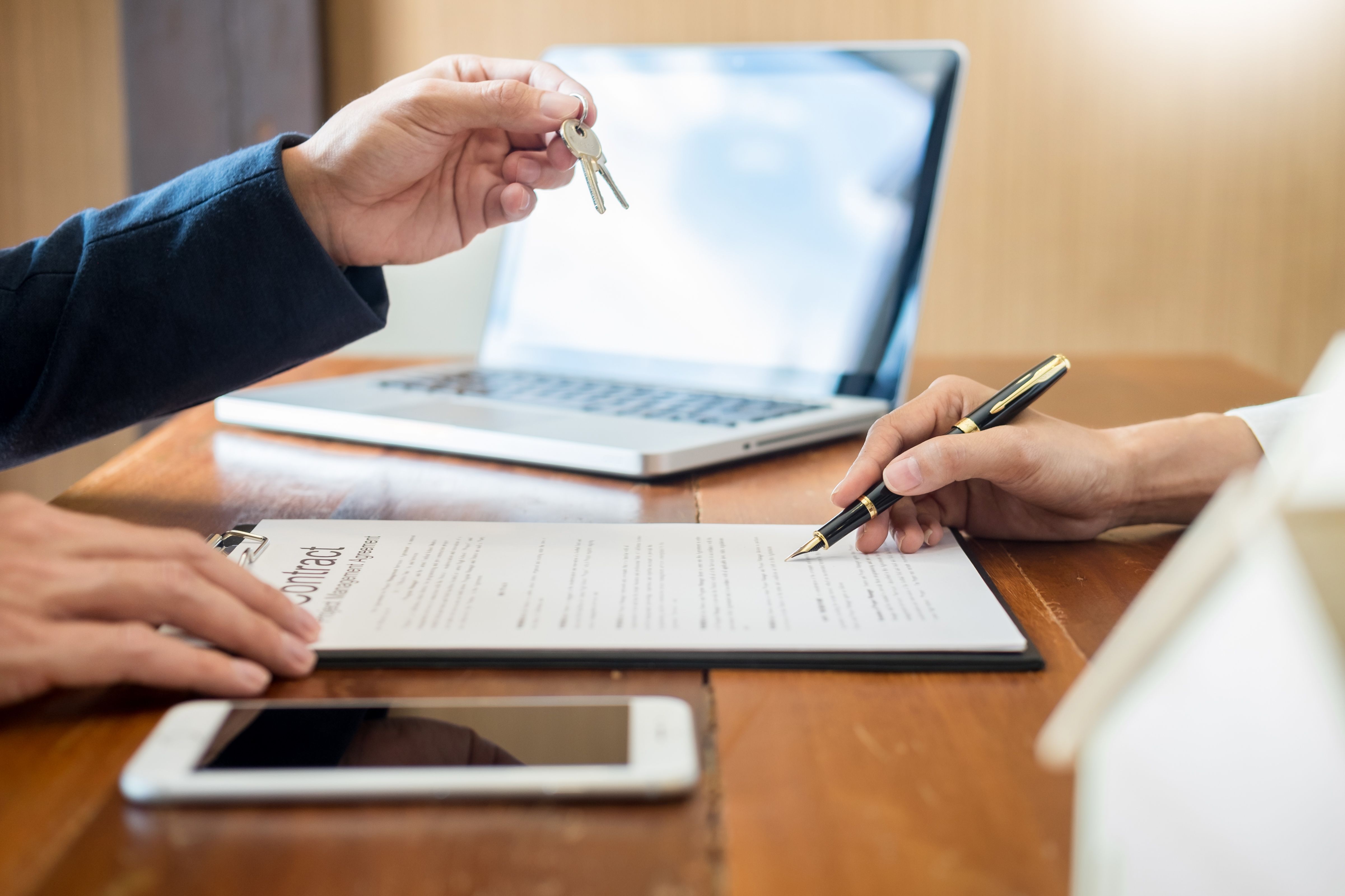 A tenant reading and signing a rental agreement while their property manager hands them the keys to their new Build To Rent home.