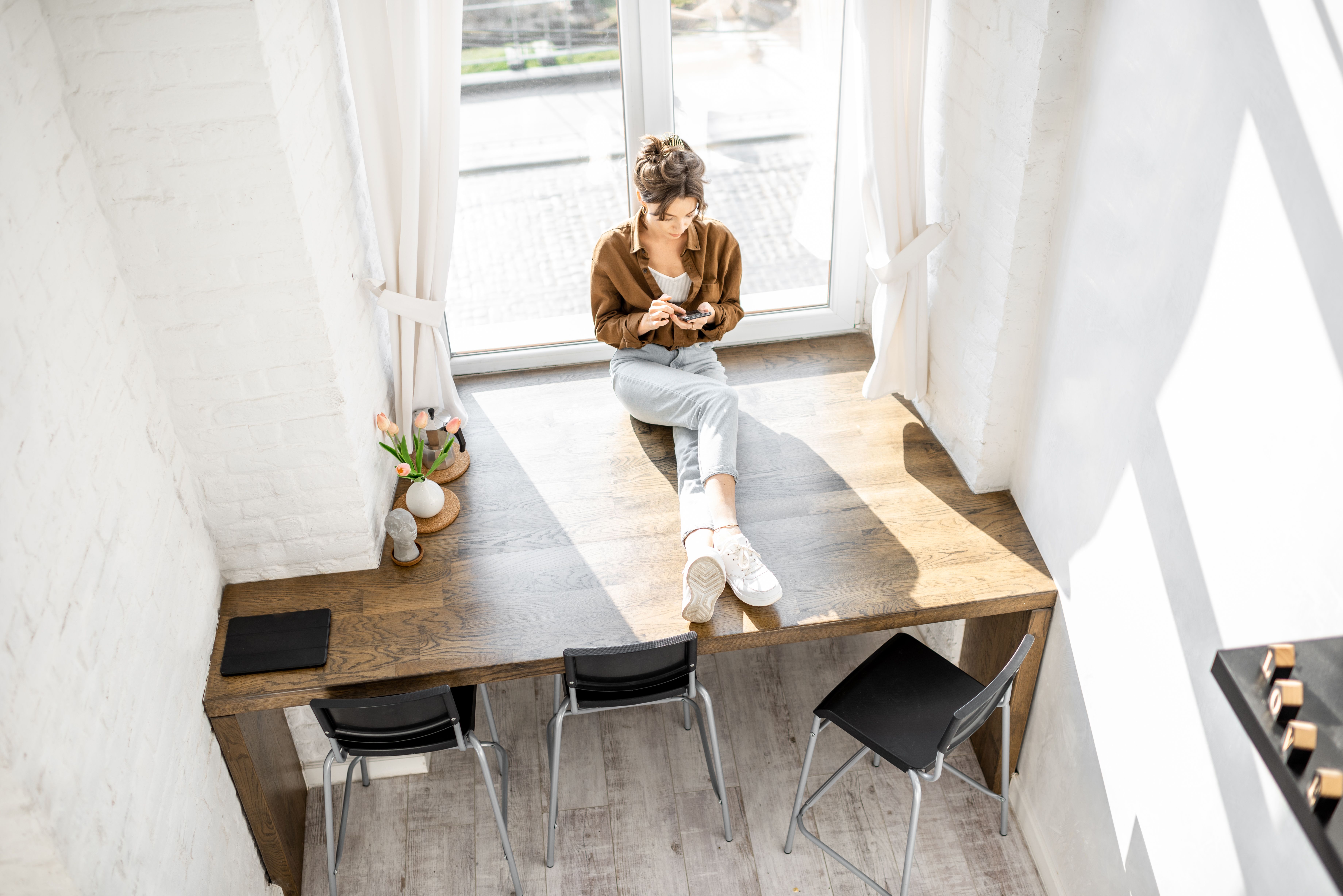 A female tenant sitting on a table and researching about repairs & maintenance at Build To Rent properties on her phone.