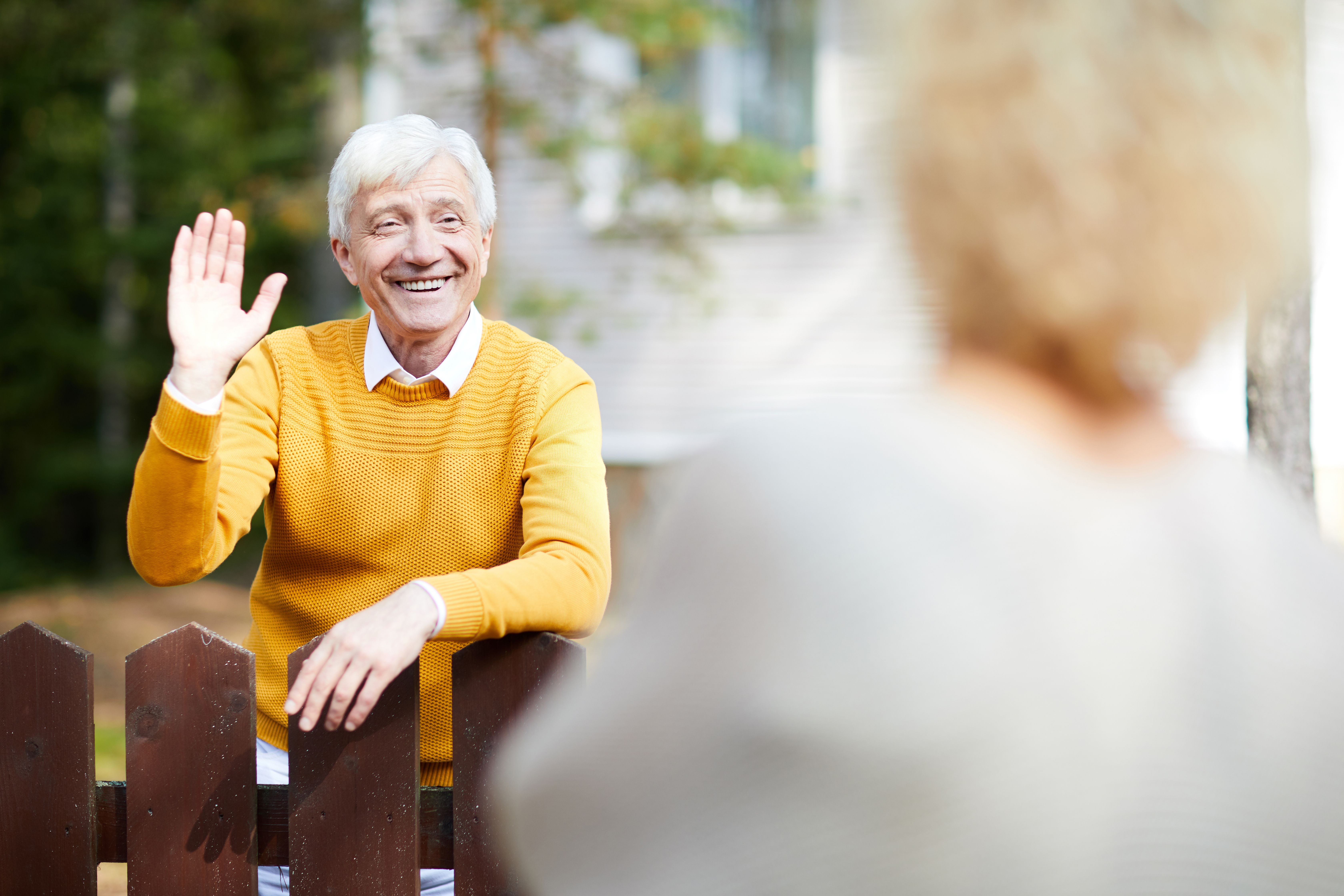 A old male landlord in a yellow sweater waves and smiles to his tenant who is move out.