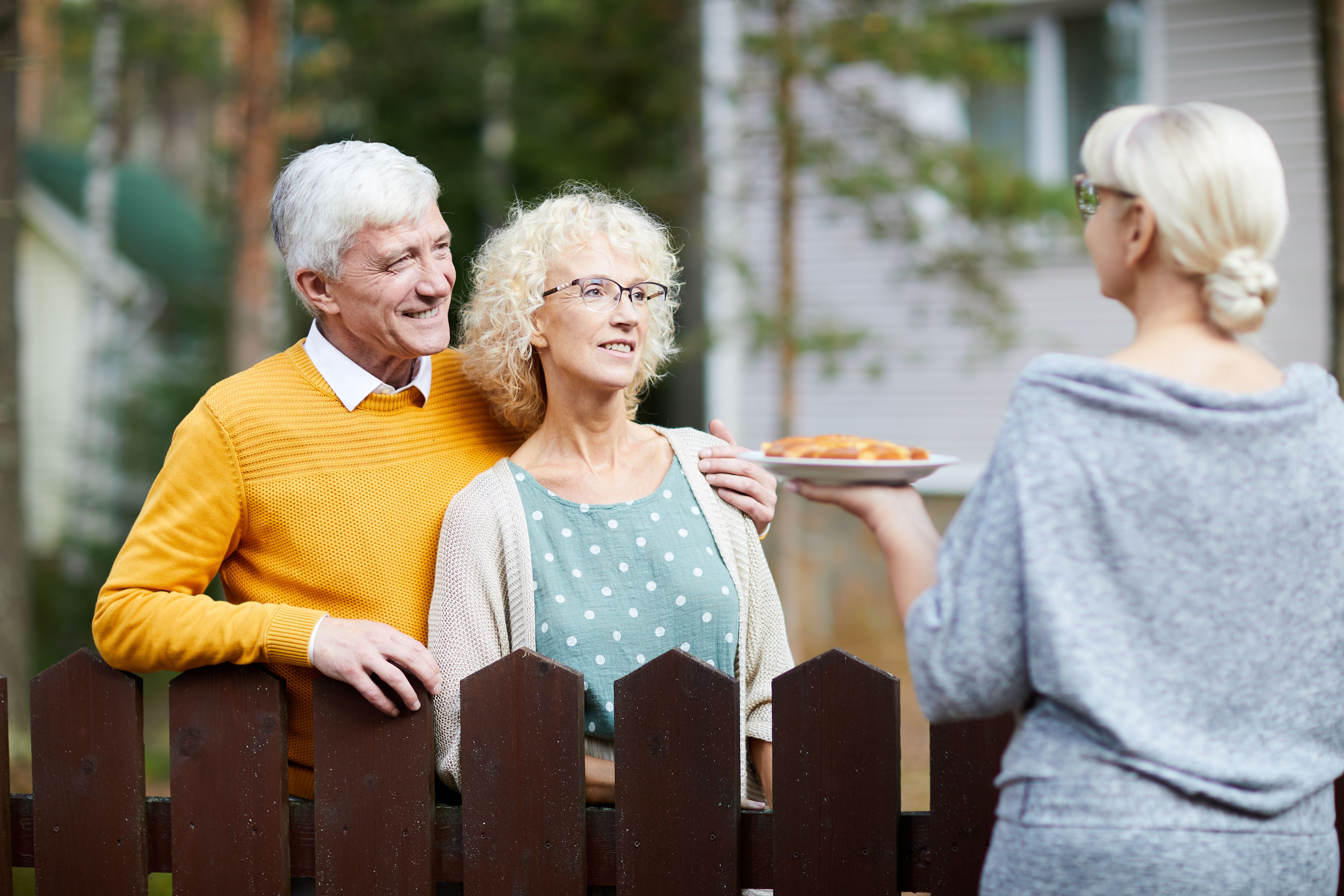 Woman giving her new neighbours homemade fresh apple pie on plate over fence