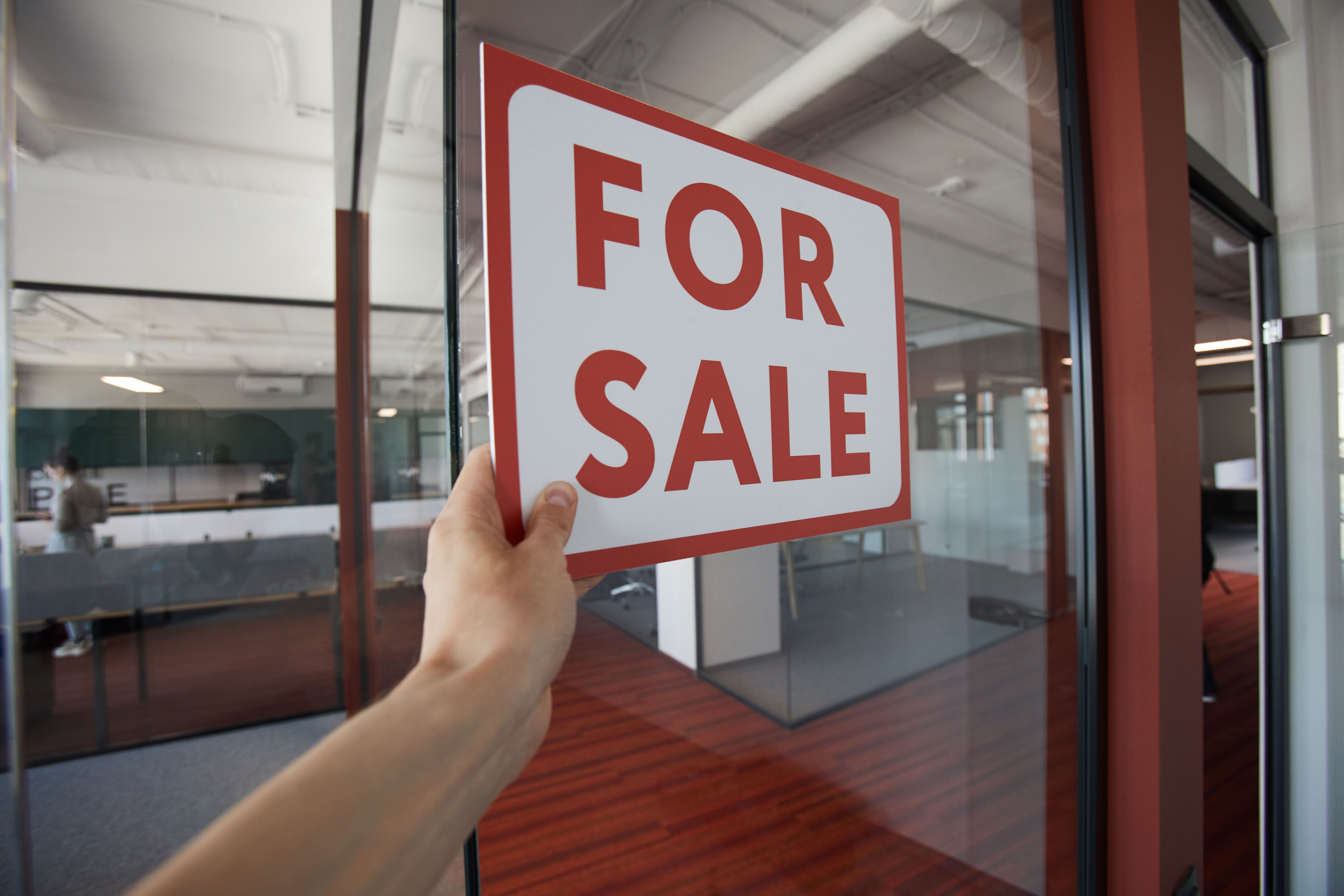 An unrecognizable man hanging the red For sale sign on the glass door of an office building
