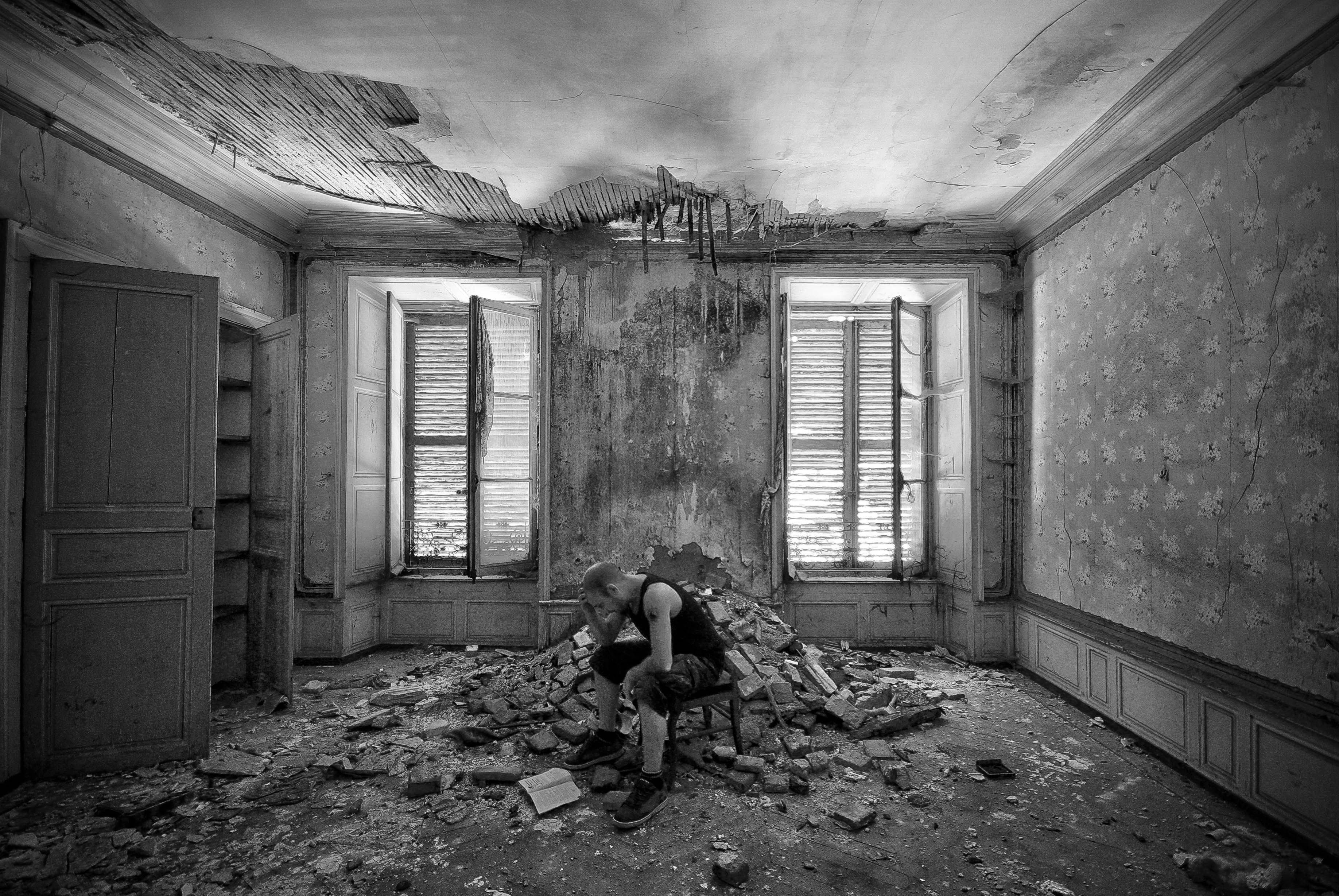 A stressful homeowner sitting alone on a chair next to a pile of brick in the middle of a refurbishing property