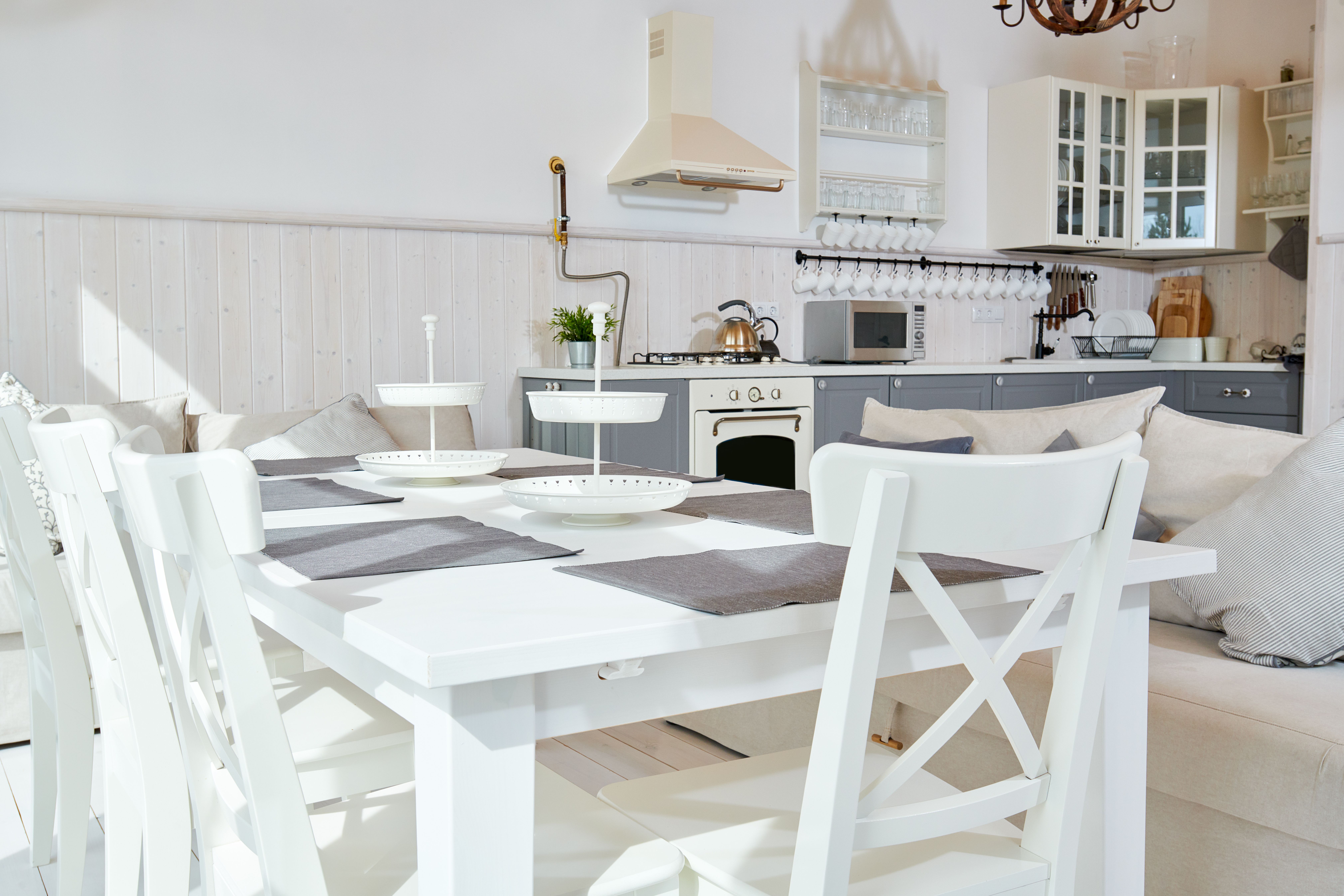 An open plan kitchen with a white table and chairs and a stove, appliances, plants and cutlery in the background 