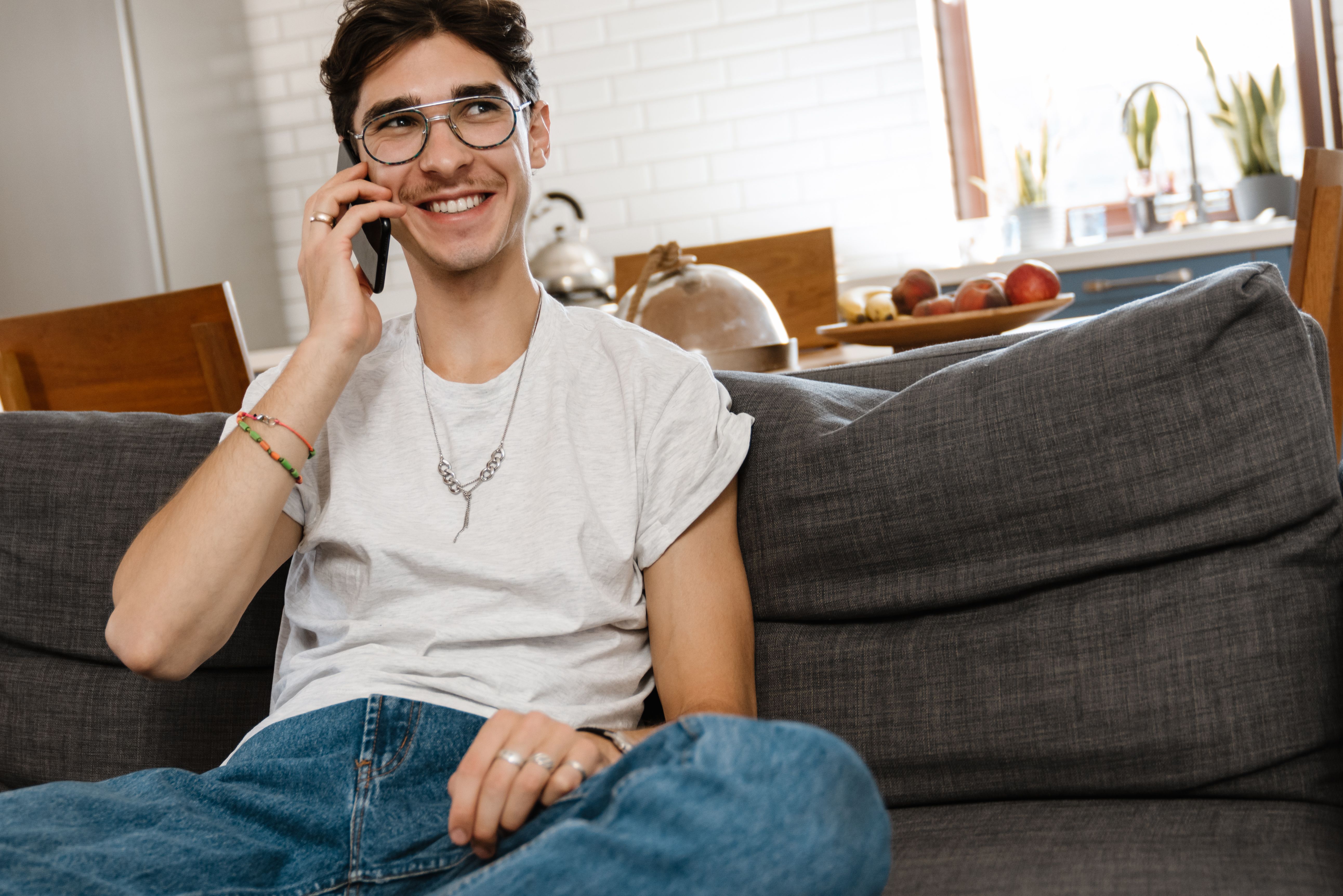 A smiling man sitting on sofa indoors at home while talking by mobile phone