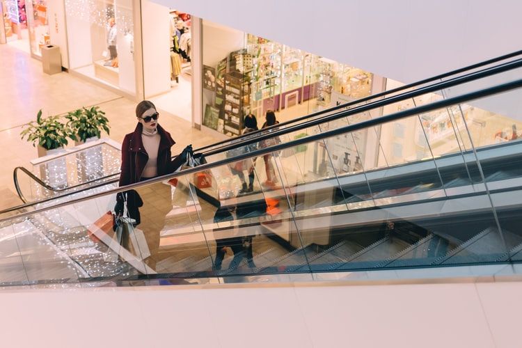 a woman in red jacket riding escalator, holding a lot of paper bags