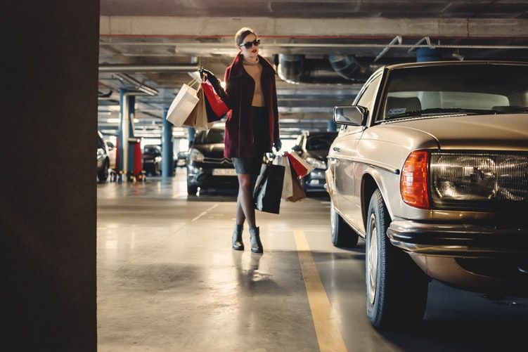 a woman carrying shopping paper bags walking towards beige car