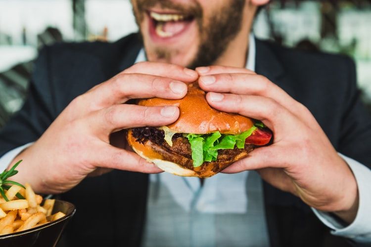 a man with smiling face holding burger bun included vegetables and meat