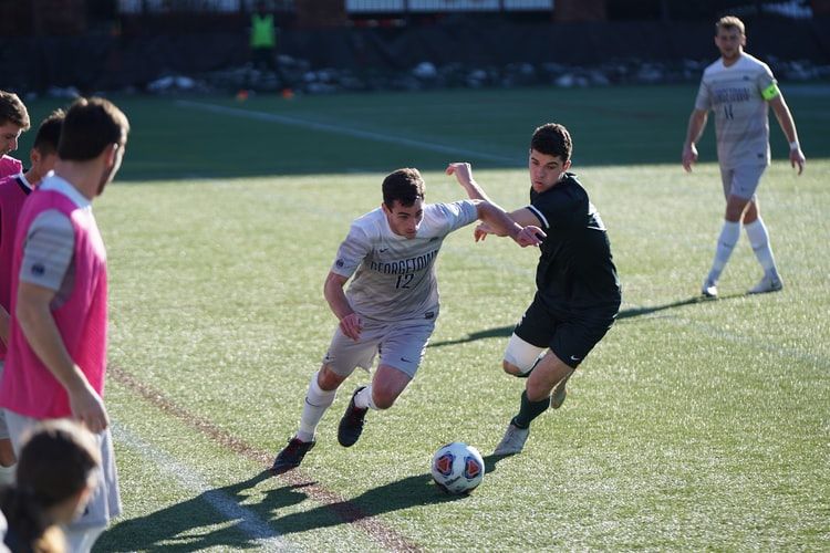 two men, one wearing black shirt, one wearing white shirt, disputing the ball