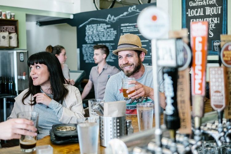 a man holding a beer mug with happy face, the woman next to him is in a conversation with others