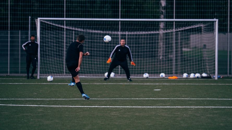 a man kicking a ball into the goal, opposite man trying to catch this ball