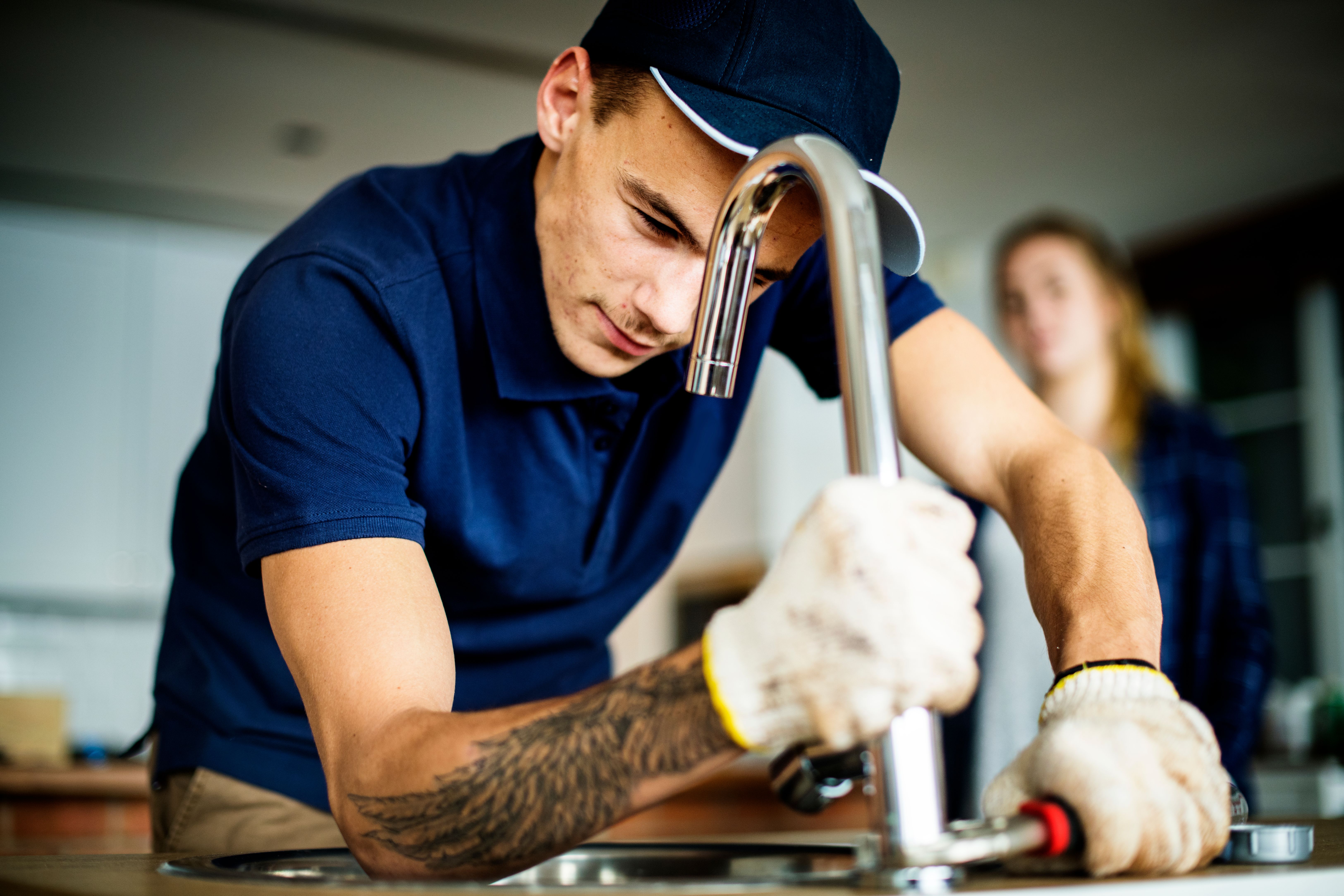 A young plumber fixing water leakage at the kitchen sink in a Build To Rent property.