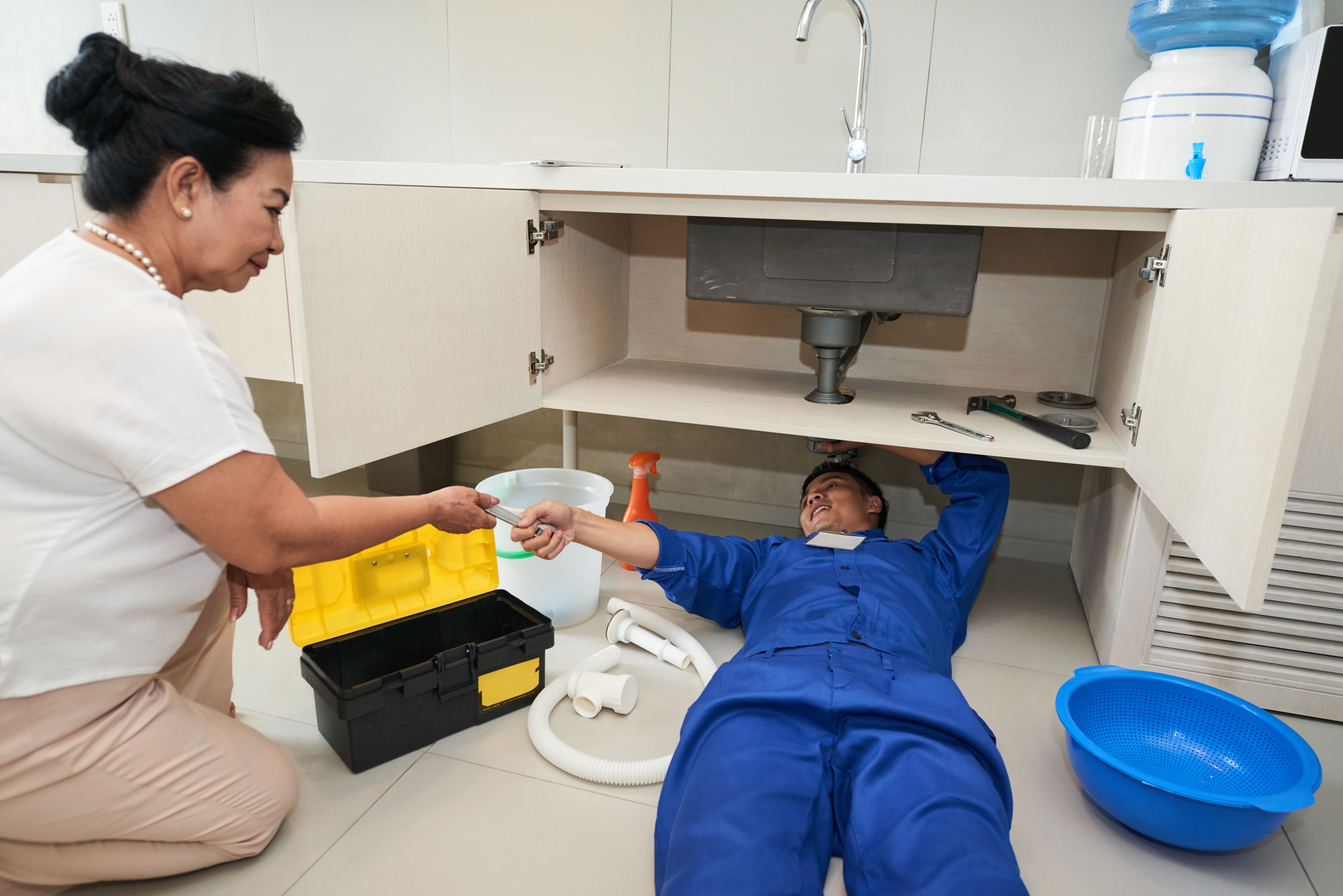 Plumber asking a senior woman to give him wrench while repairing a leaking pipe