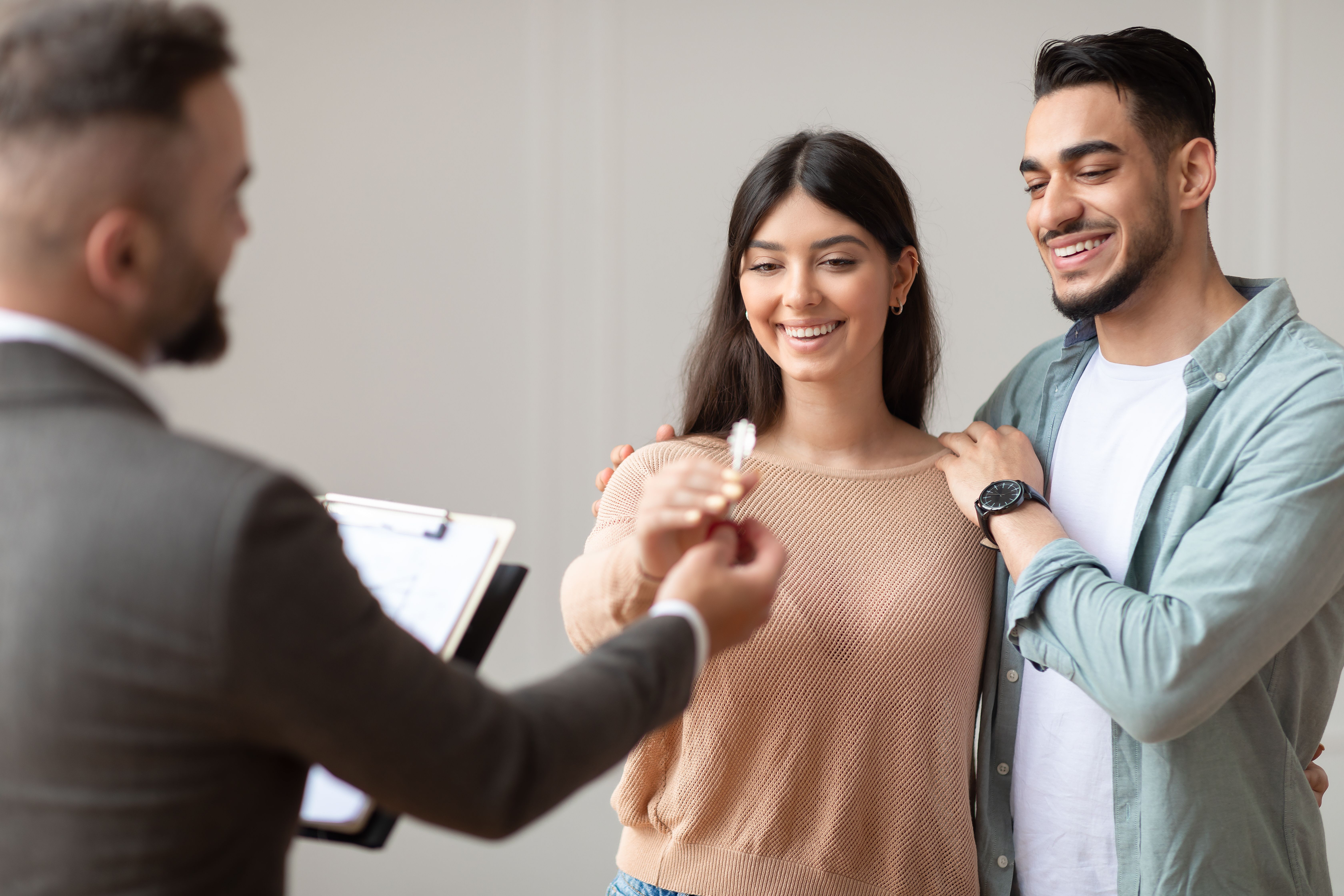 a real estate agent giving keys to a young couple with happy face