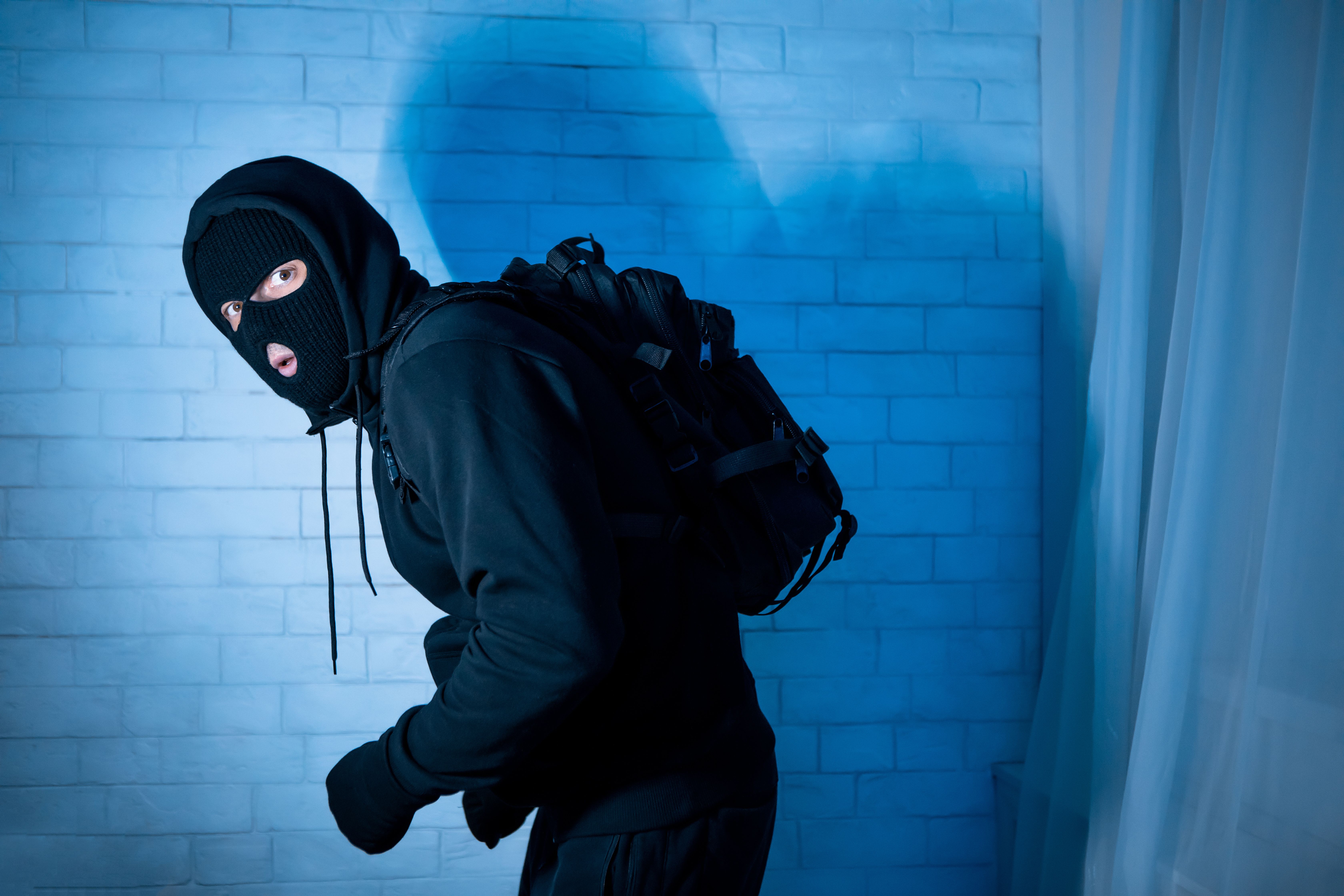  A sneaky intruder wearing a black balaclava hat lurking in the dark