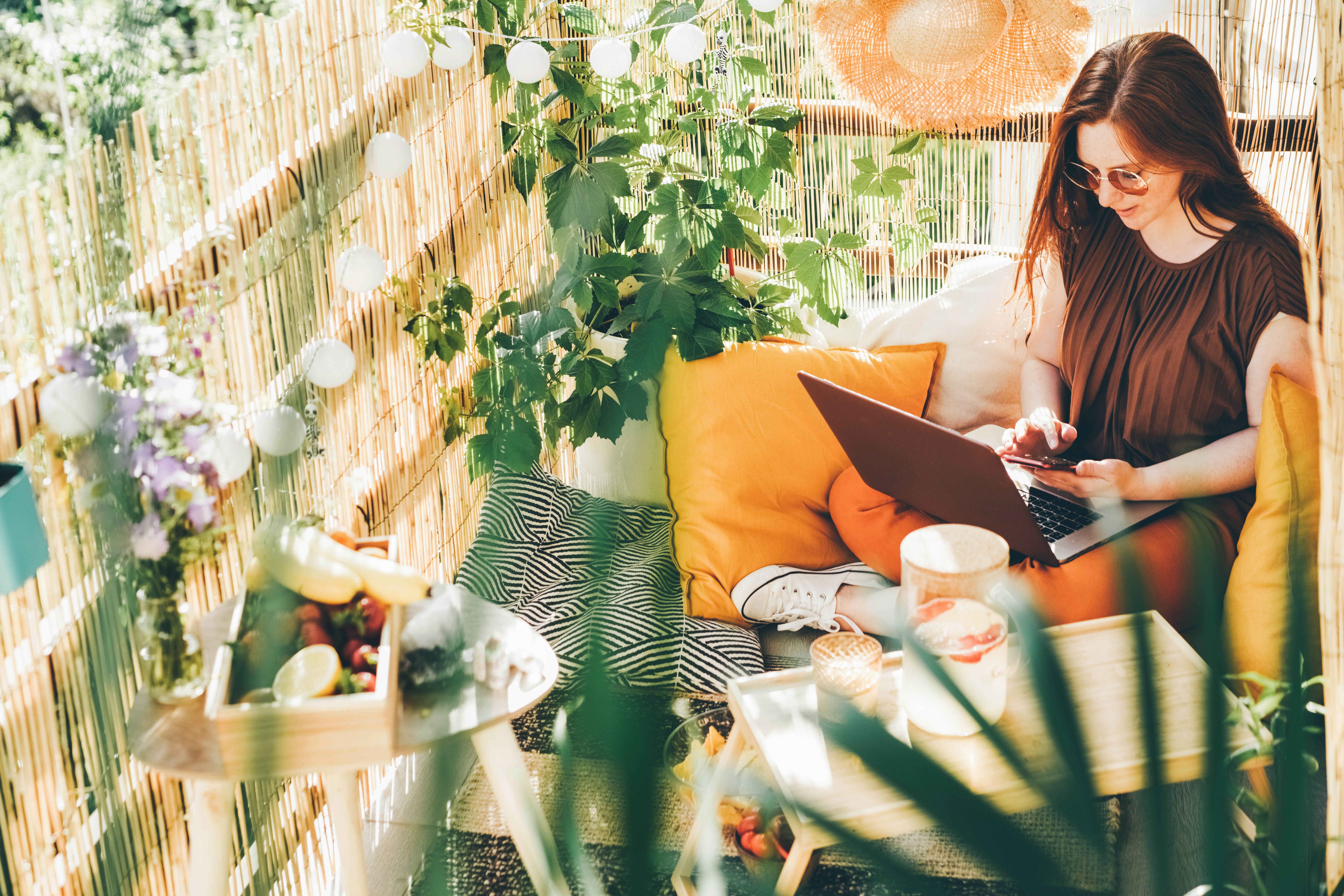 A female tenant wearing sunglasses and working from her sunny balcony in a Build To Rent apartment.