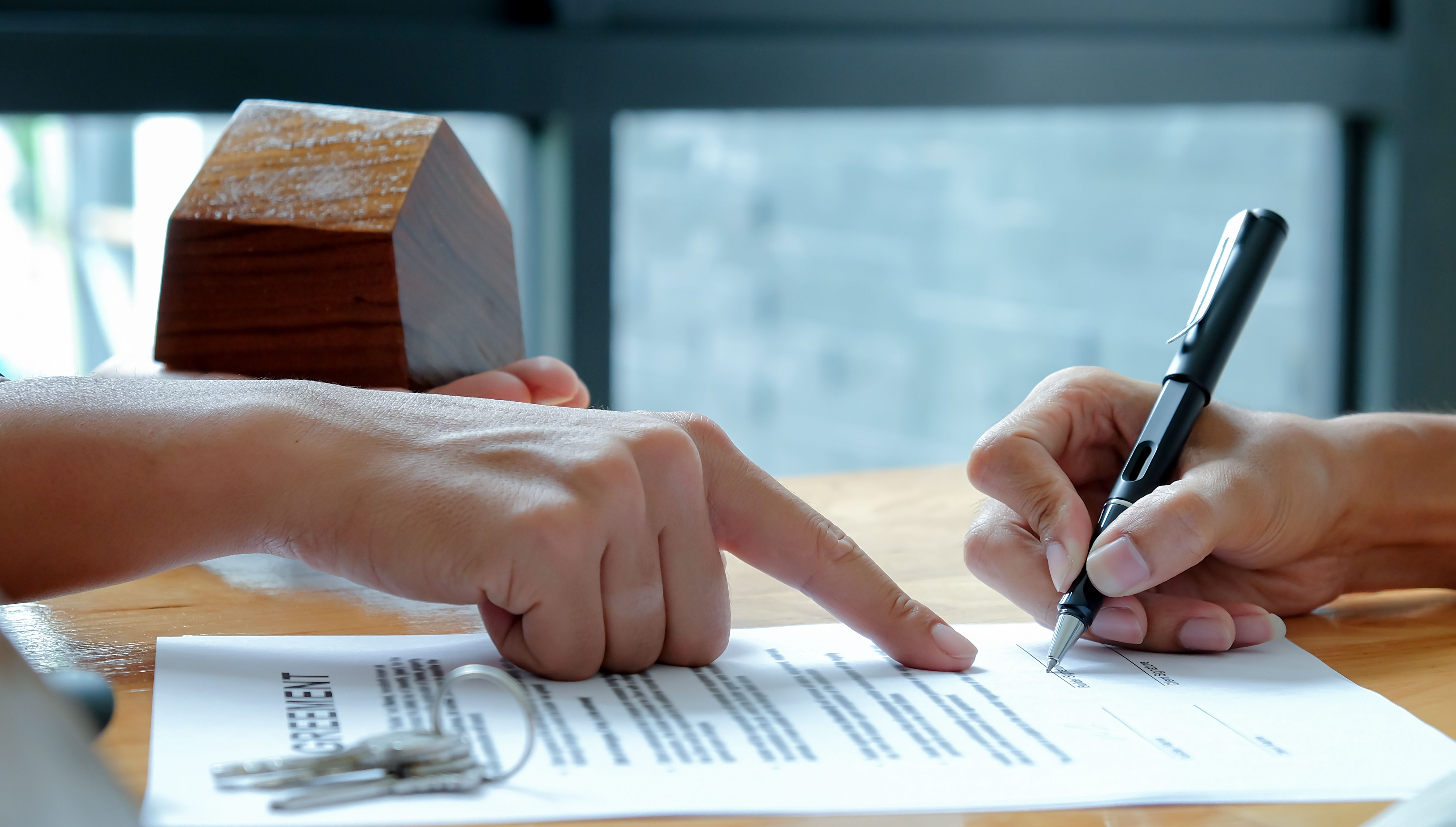 Close-up shot of a person pointing to a document for another person to sign.