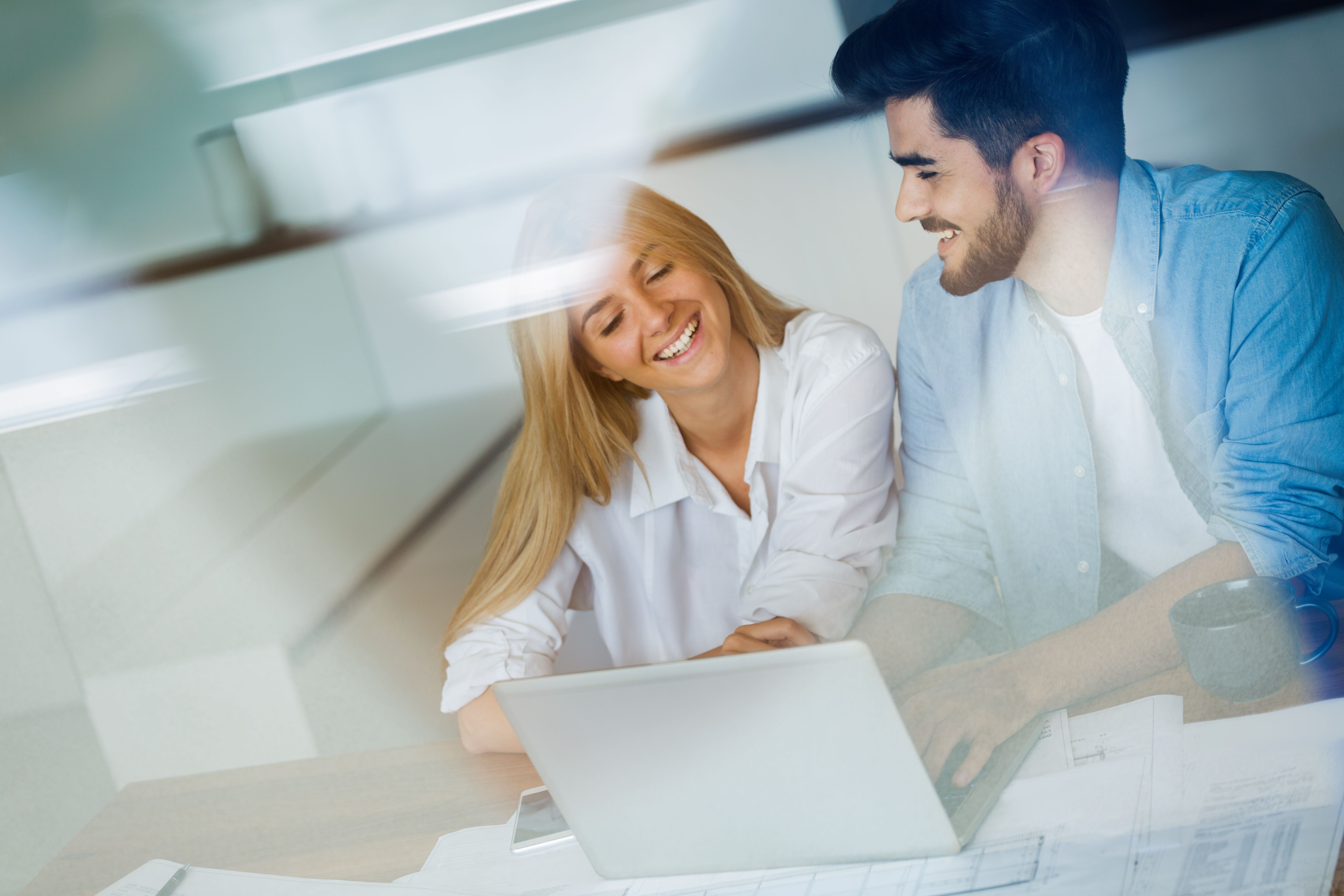 A happy couple sitting in their Build To Rent home and using a laptop to calculate their monthly bills with documents on the table.