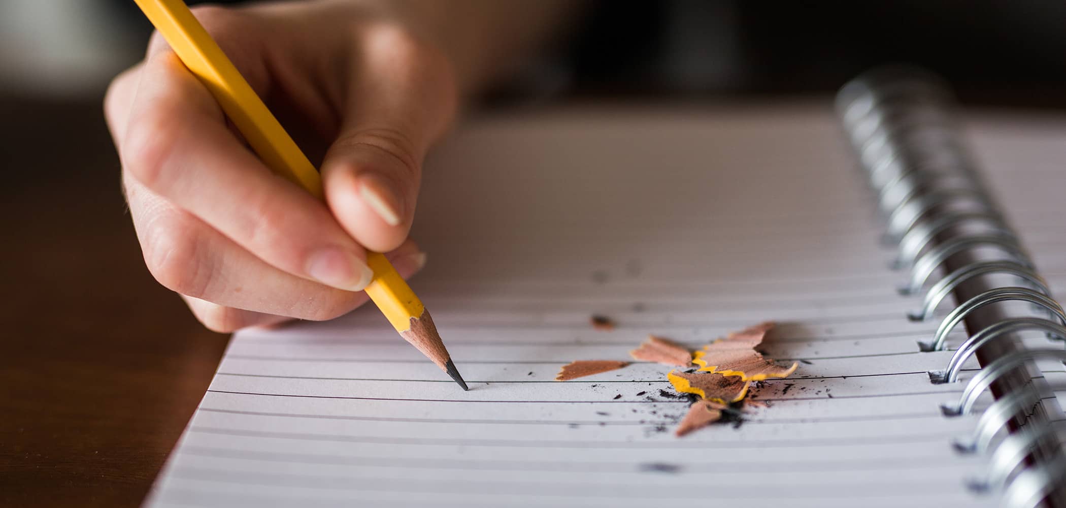 A person writing with a pencil on a notebook