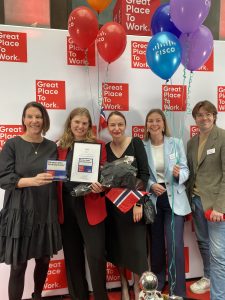 A group of Cisco Norway employees stand holding Norwegian flag and balloons in front of Great Place to Work step and repeat.