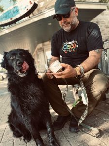 Black dog licking mouth and man in "Somos Cisco" shirt eating ice cream.