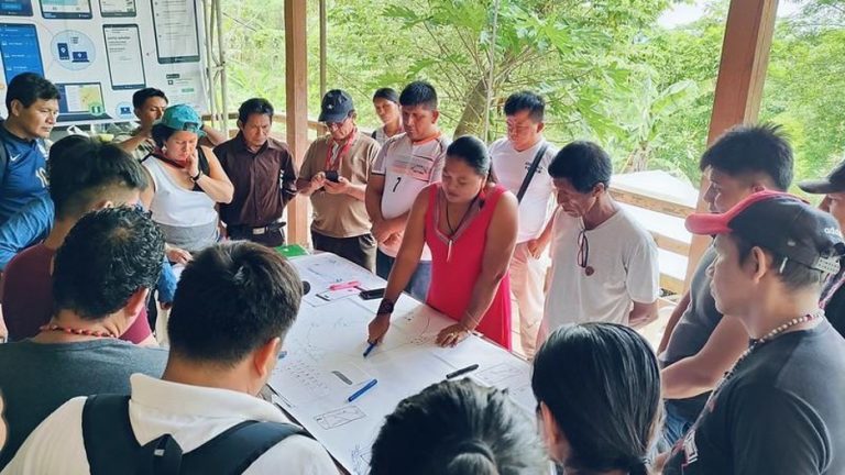 A large group of people looking at a map on a table together, with green trees behind them
