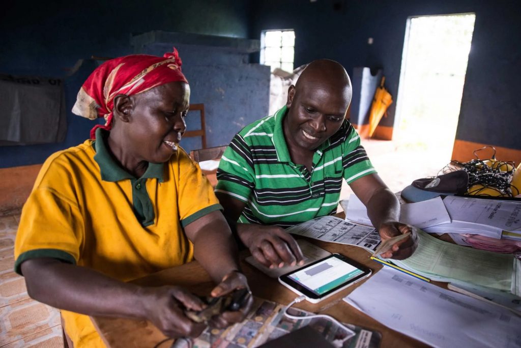 Two people wearing bright clothing, sitting inside at a table using technology