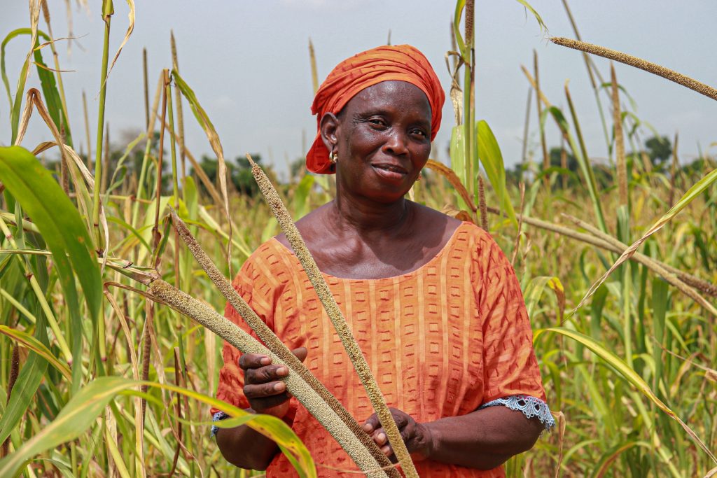 A woman farmer wearing bright orange, standing with her harvest