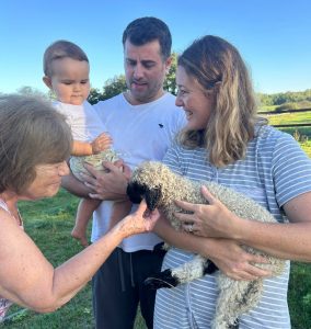 Sebastian holding his baby with his wife holding a baby lamb in a field