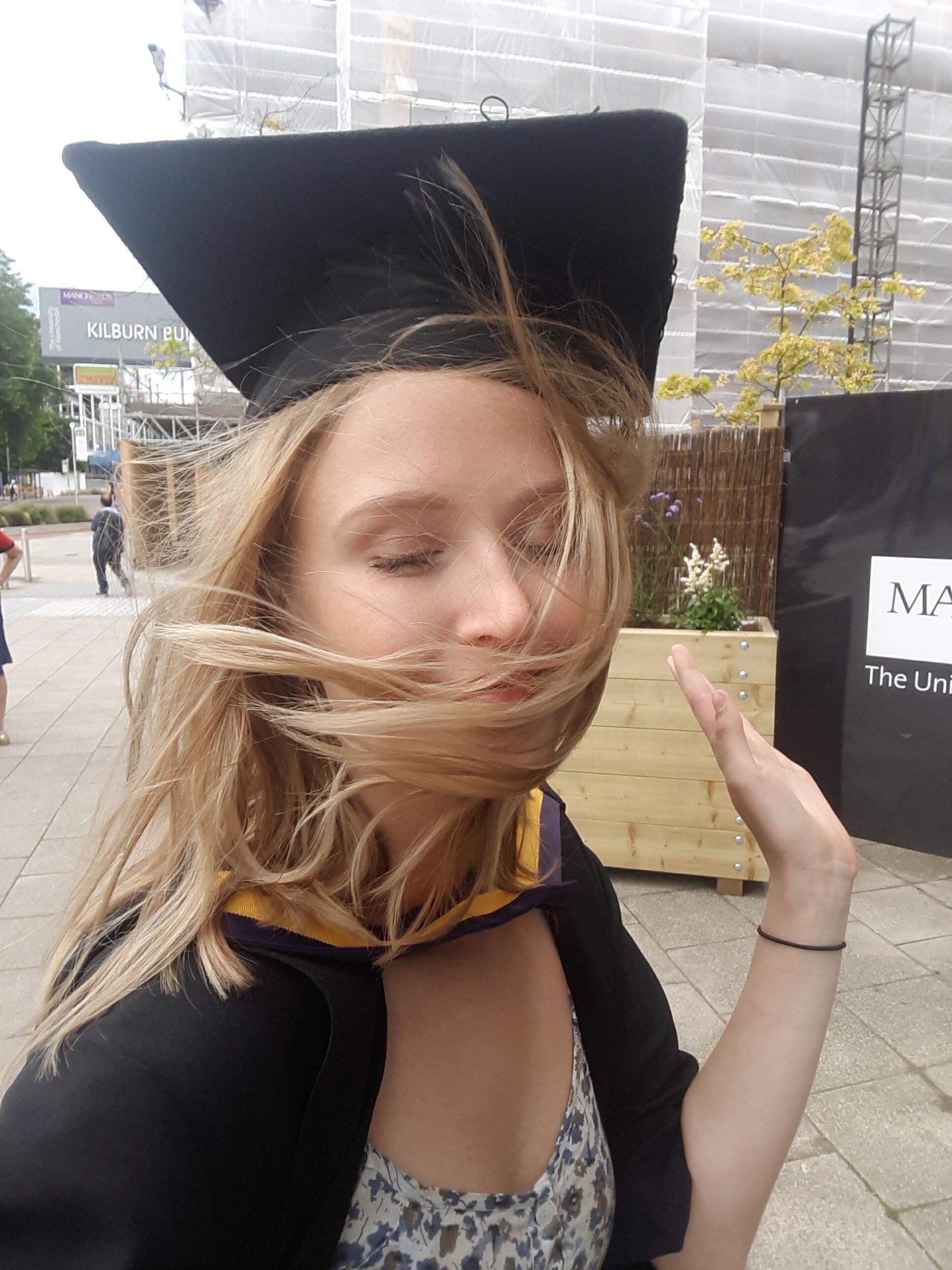 Marte on Graduation Day wearing a cap and gown with wind blowing her hair over her face.