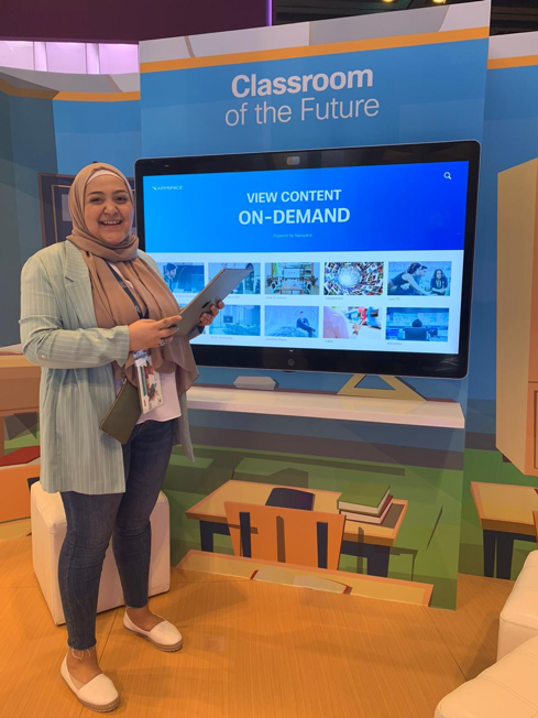 Haya Alzeer stands in front of a Webex Board and a wall that says Classroom of the Future.