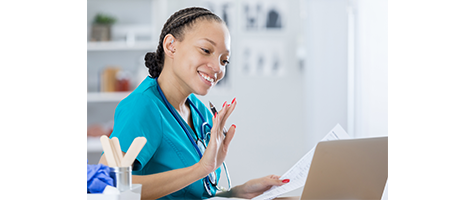 Healthcare Reimagined: Creating a Better Remote Care Experience. Young nurse greeting online patient on her computer waving high with one hand and looking at medical papers on the other side