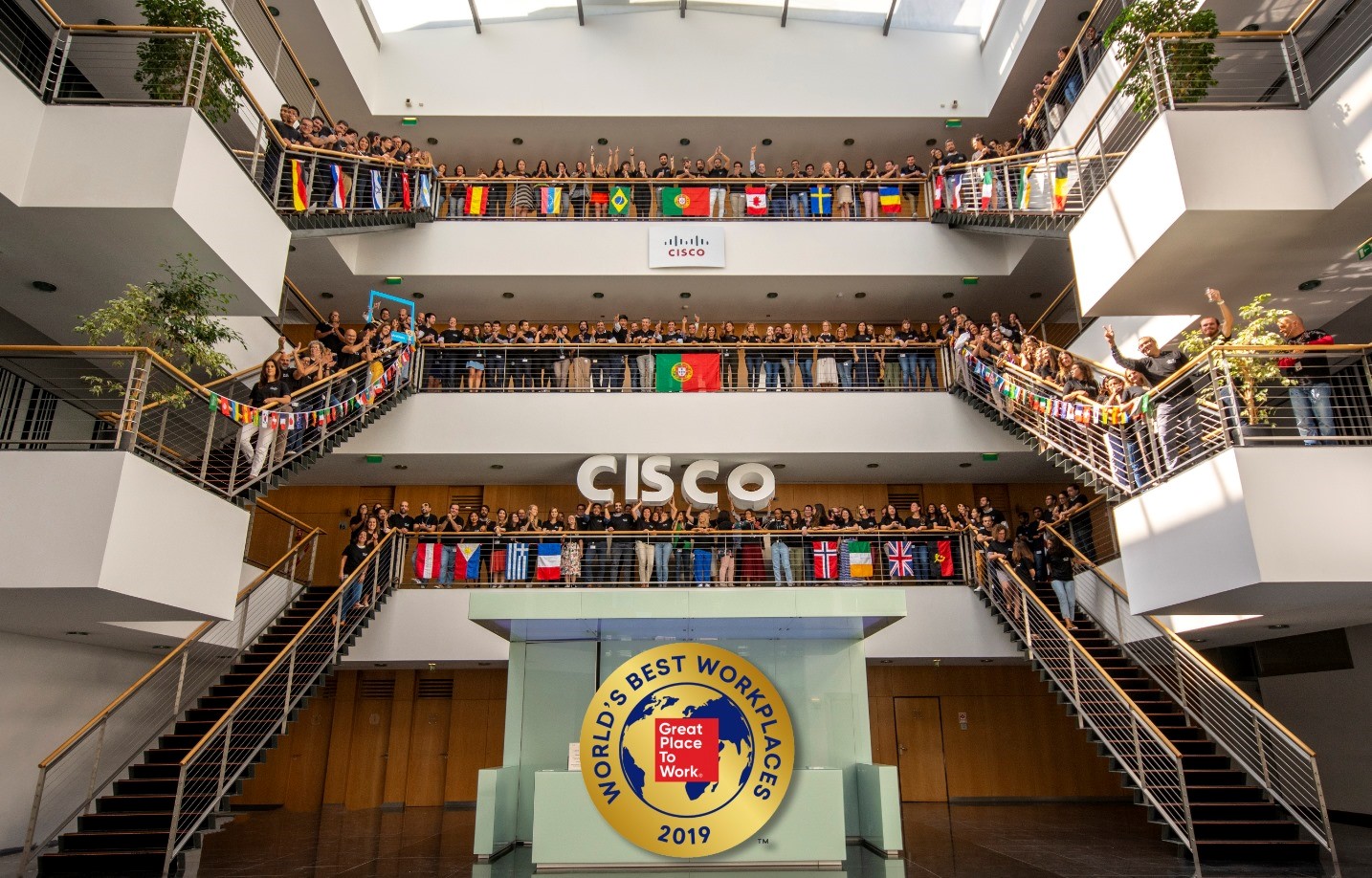 Cisco Lisbon employees standing in the foyer on 3 different levels with over 35 flags for the employees countries and a large sign that has 2019 World's Best Workplaces written across a globe.