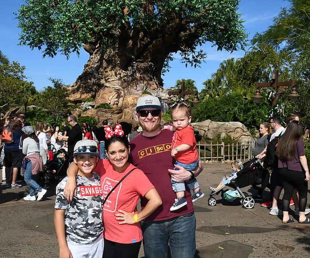 Nic and his family smile wearing Cisco gear in front of the Tree of Life at Disney World.