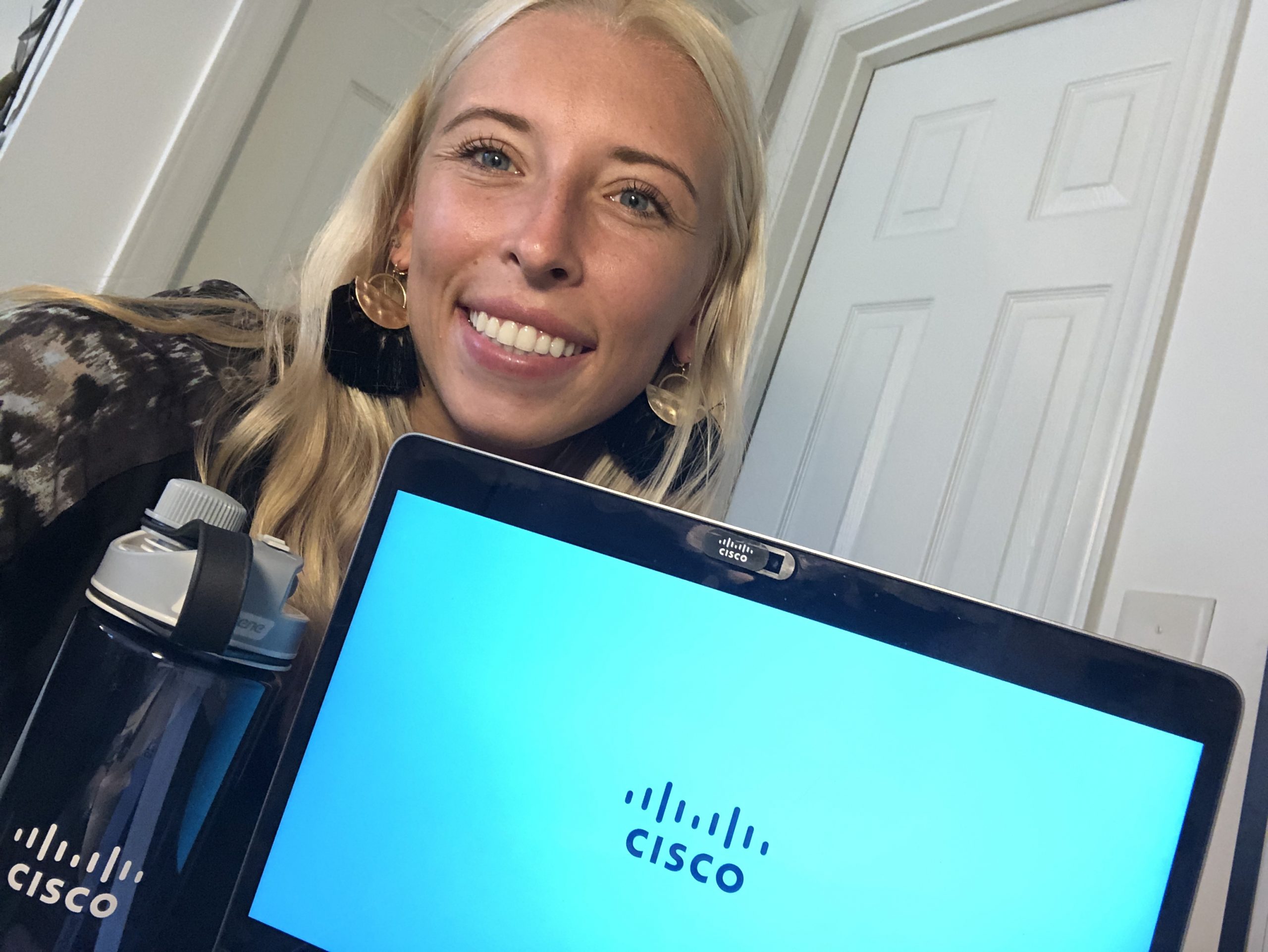 Courtney smiles behind her Cisco laptop and branded water bottle.