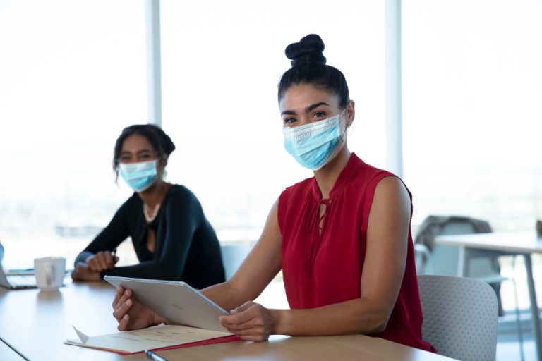 Two women sitting at a table wearing face masks