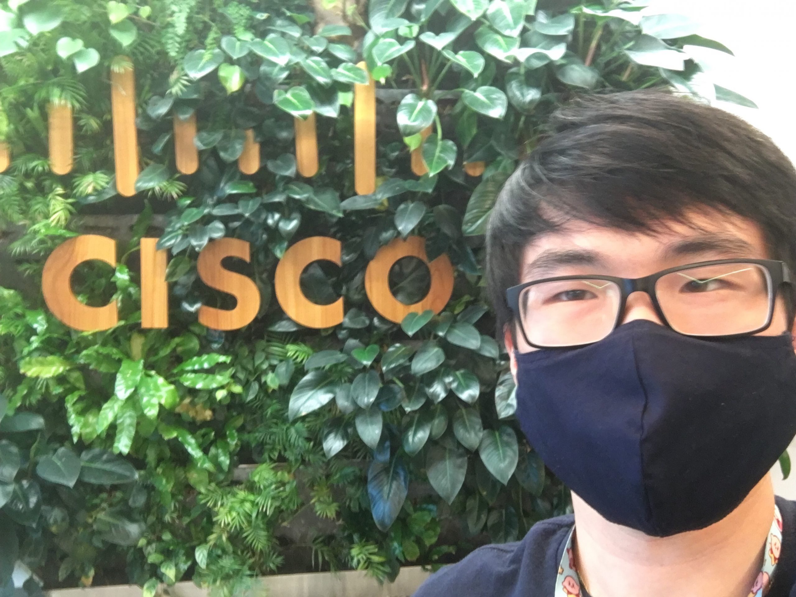 Bryce with mask in front of Cisco sign. 
