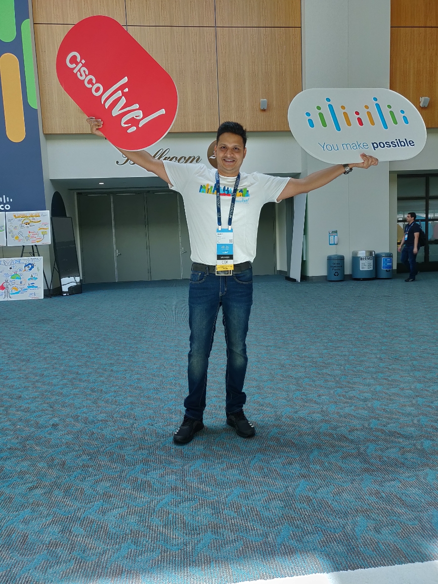 Rohit holds up a Cisco Live and "You Make Possible" signs in each hand at an event.