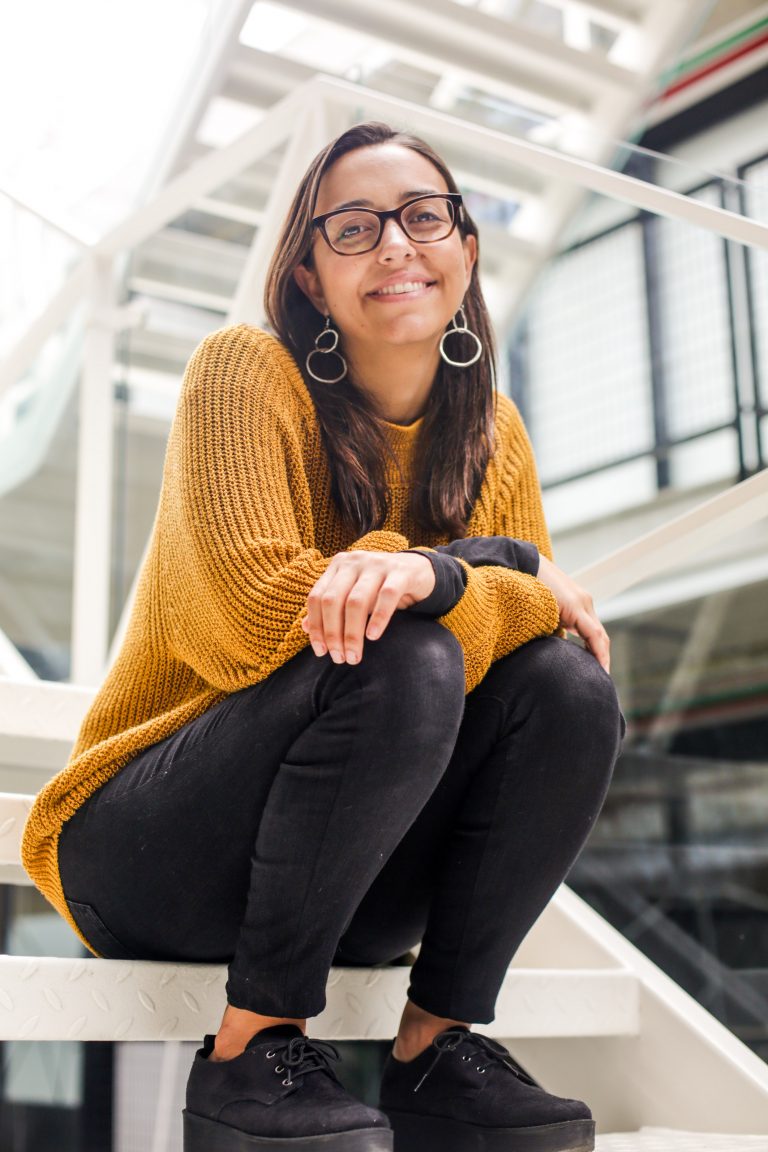 A young woman wearing glasses sits on some stairs 