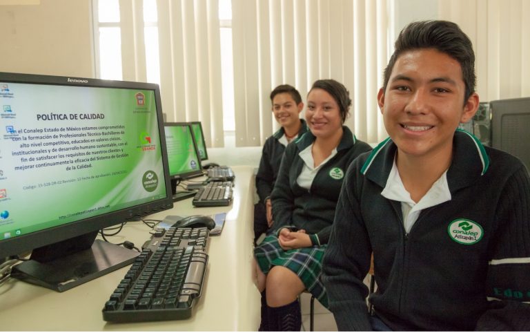 Students sitting in a computer lab and smiling at the camera.