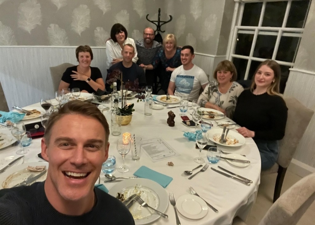 Jessie Pavelka selfie and team behind him at dinner table.